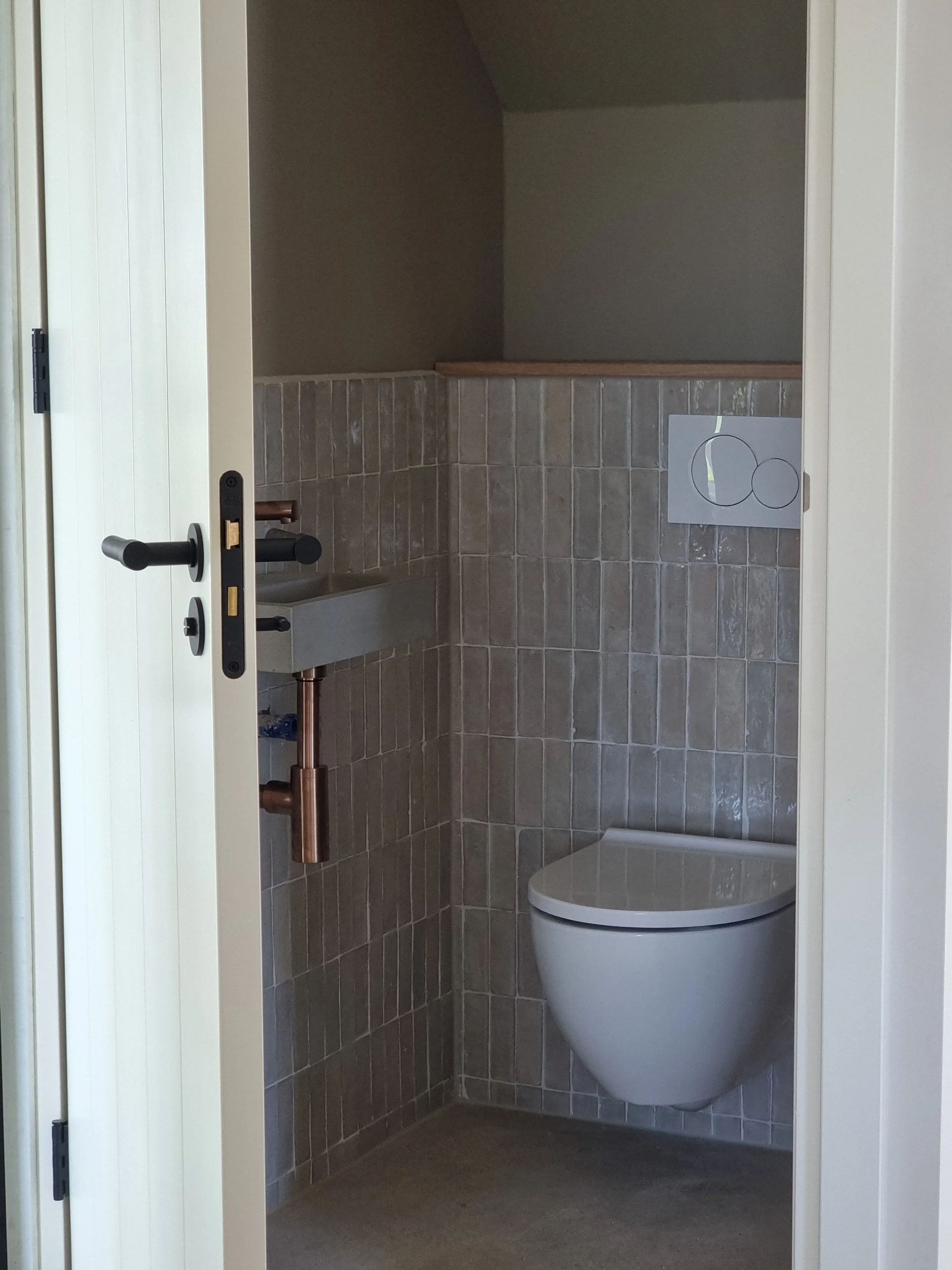 Moderne toiletruimte met wandcloset en klein wastafeltje, betegeld in fijne beige tinten, met een eenvoudige schematische tekening op de muur.