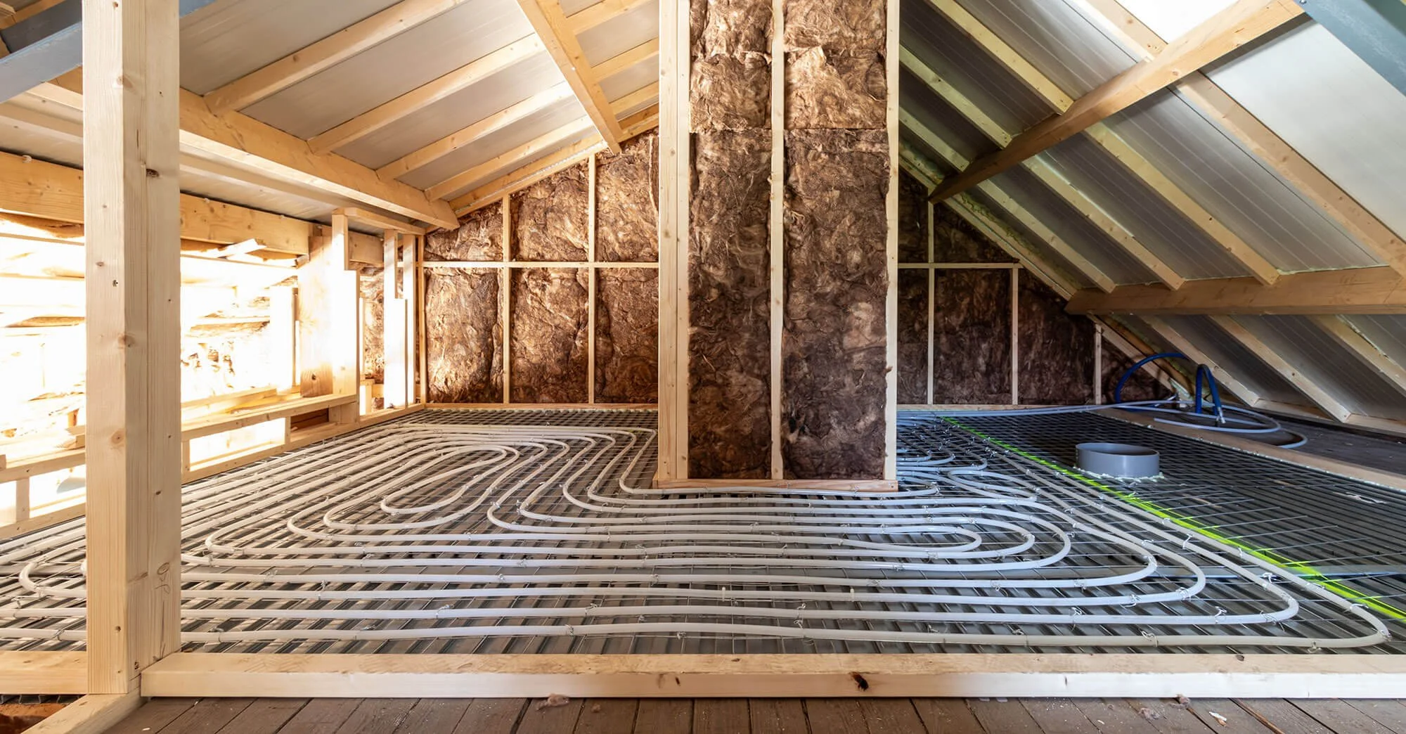 Binnenkant van een zolder met een nieuw aangelegd vloerverwarmingssysteem, houten wanden en geïsoleerde muren.
