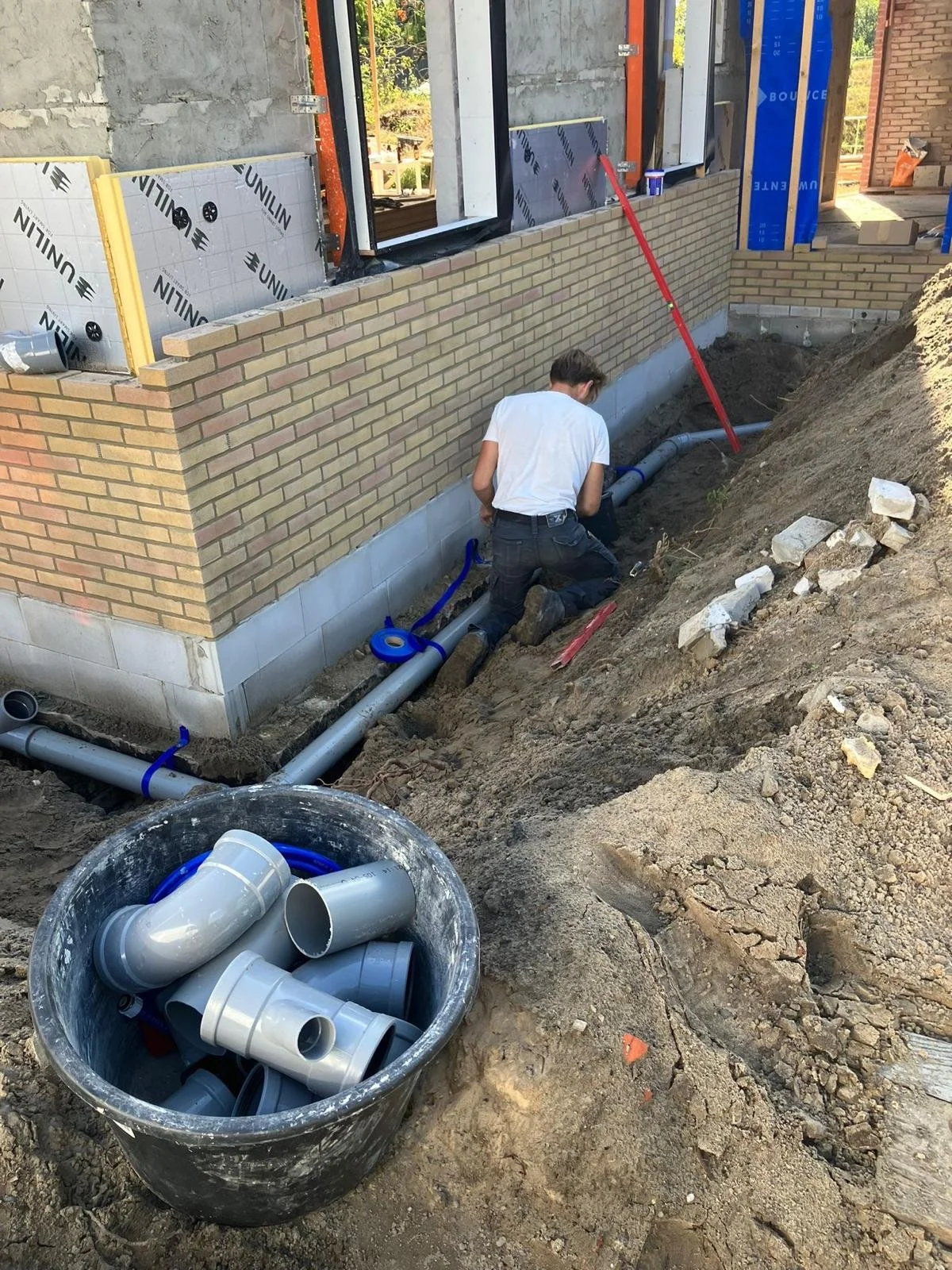 Een bouwwerker legt geventileerde PVC-afvoerpijpen aan bij een huis met bakstenen muur in aanbouw.