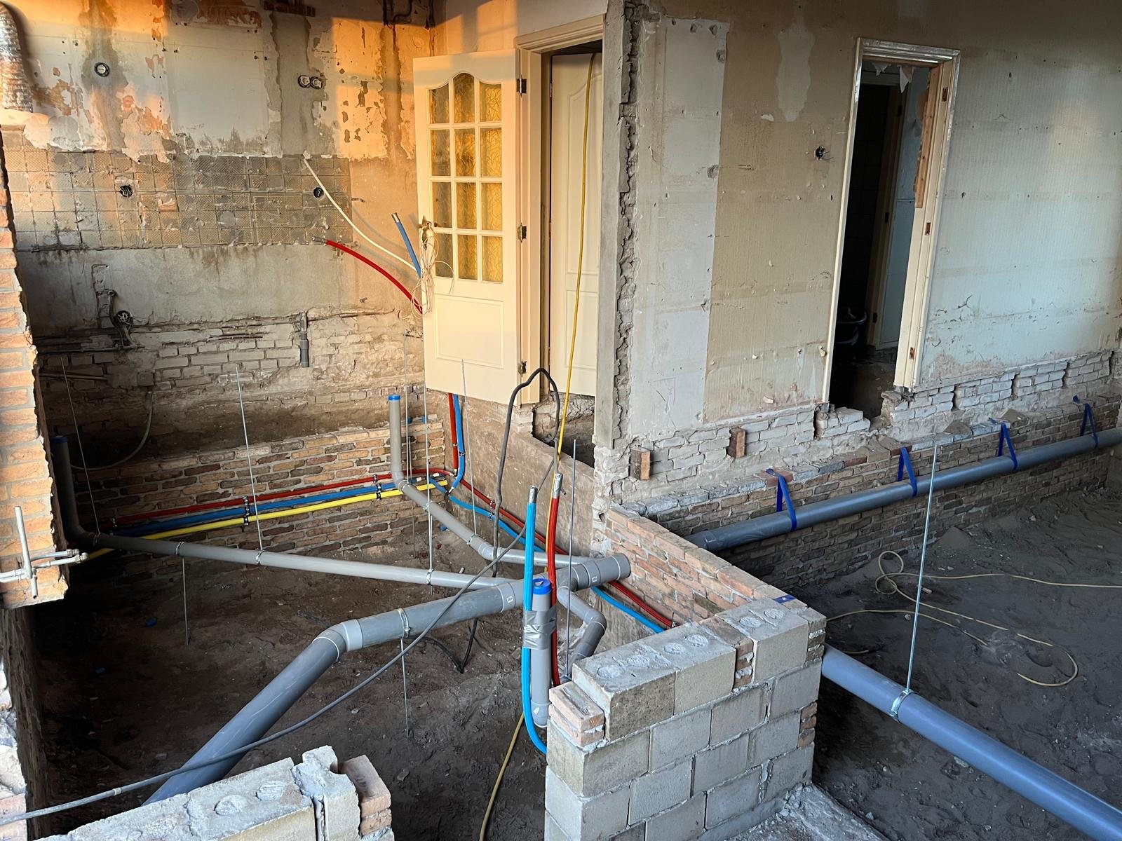 Binnen een bouwplaats, geïnstalleerde elektrische en waterleidingen in een woning onder renovatie, met onafgewerkte muren en vloeren.
