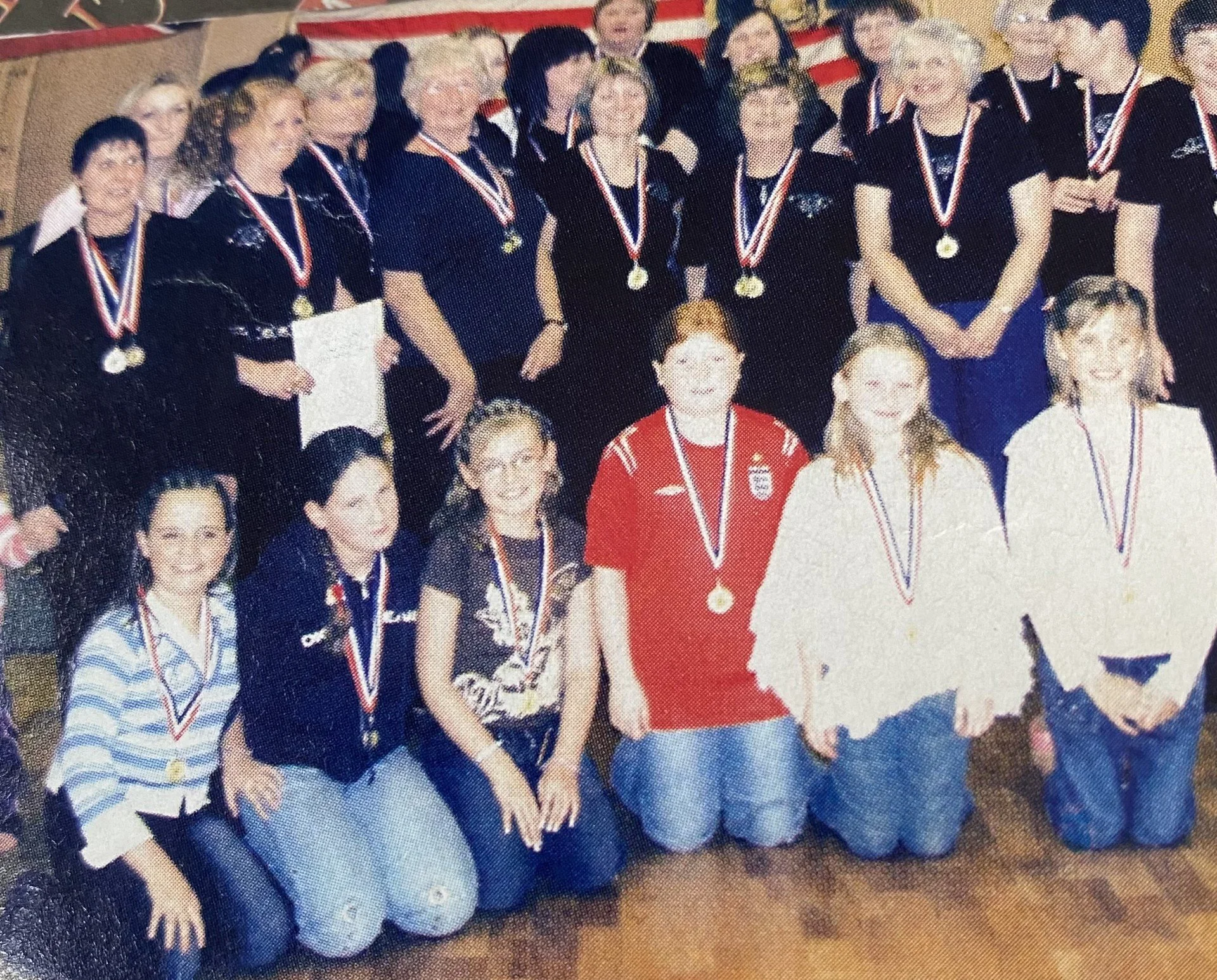 Group of young women and girls, some wearing medals around their necks, posing for a photograph indoors, likely after a sports event or competition.