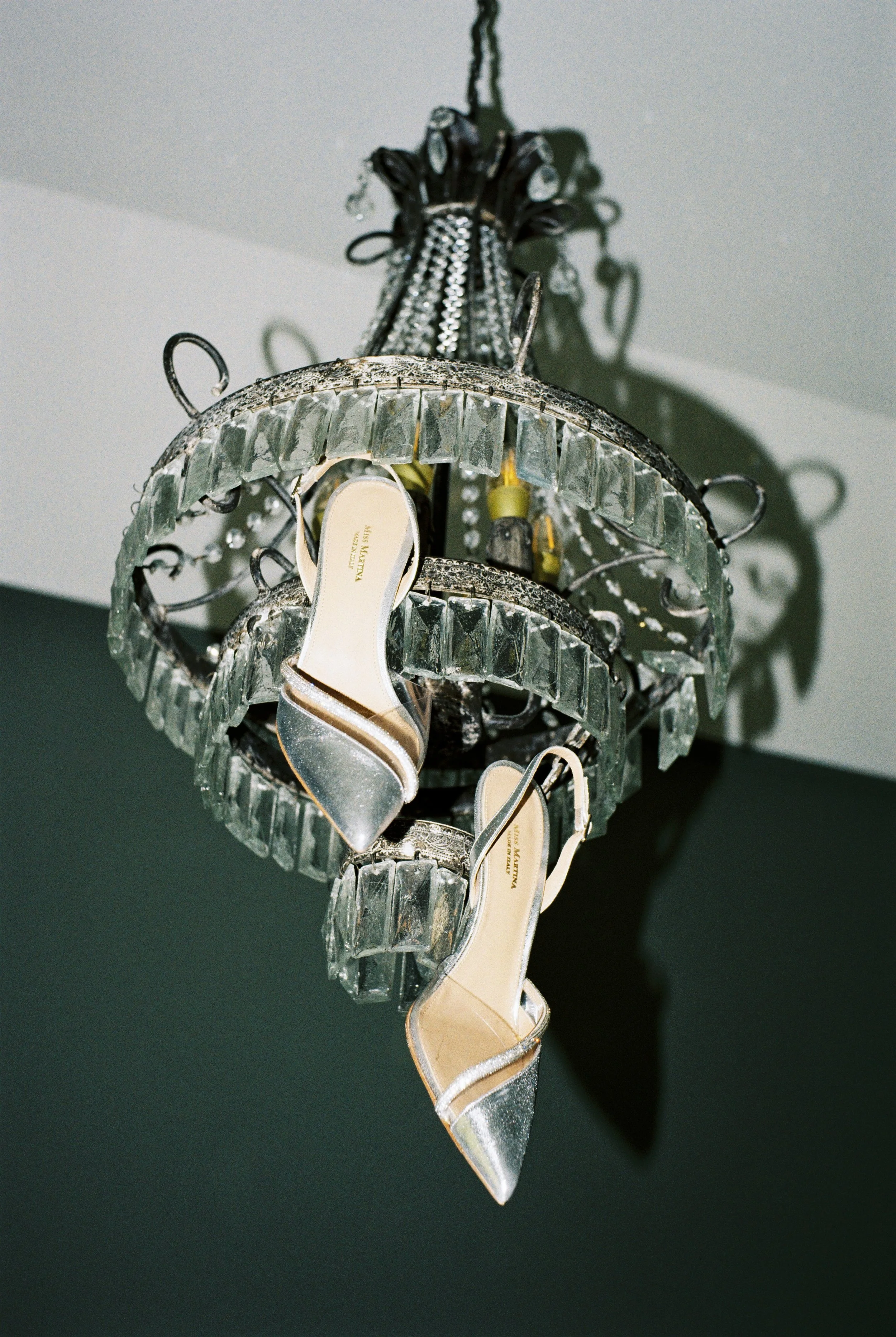 Un lampadario decorato con cristalli e una scarpa con tacco aperto appesa ad esso.