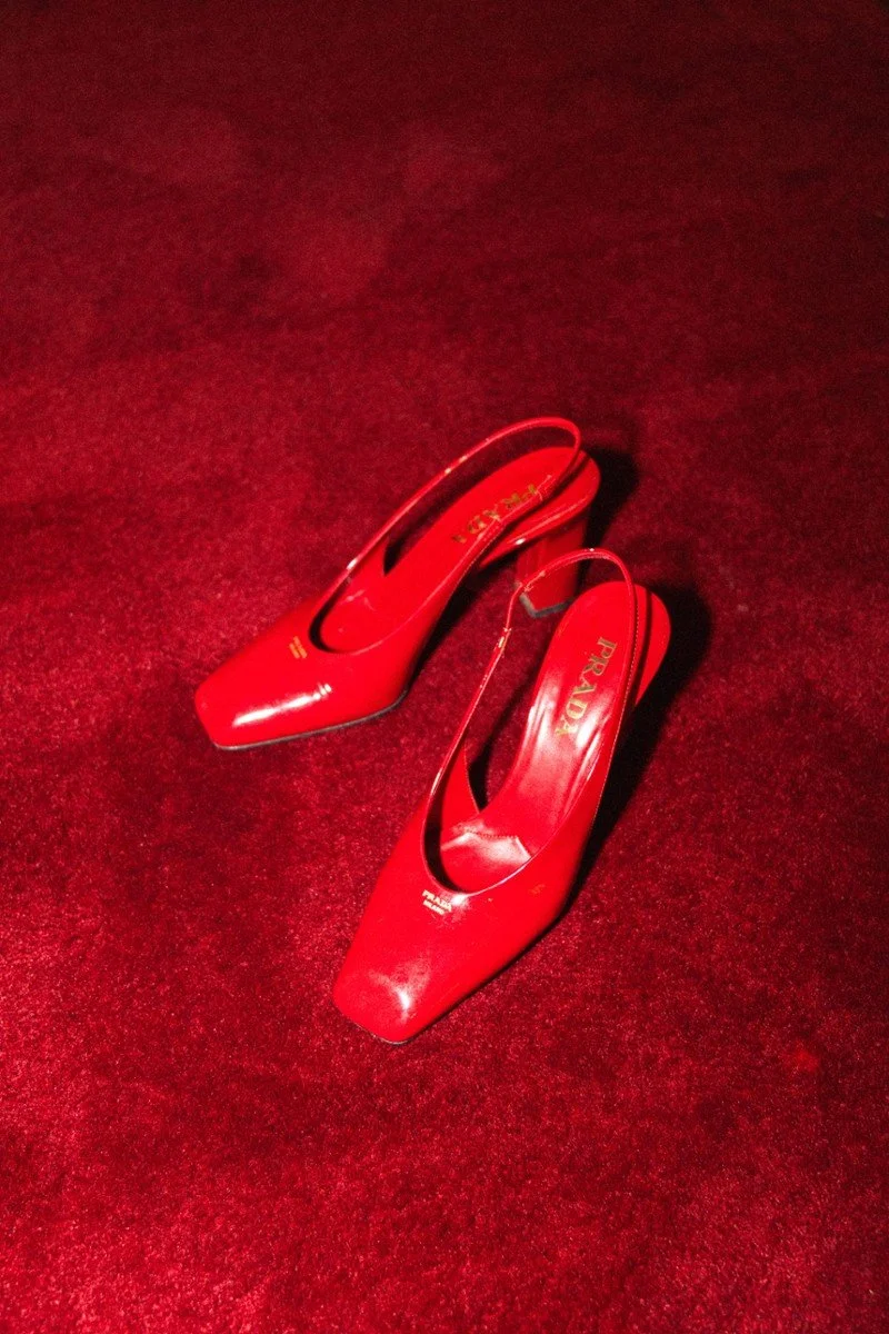 Un paio di scarpe rosse a punta con tacco alto poggiate su un tappeto rosso.