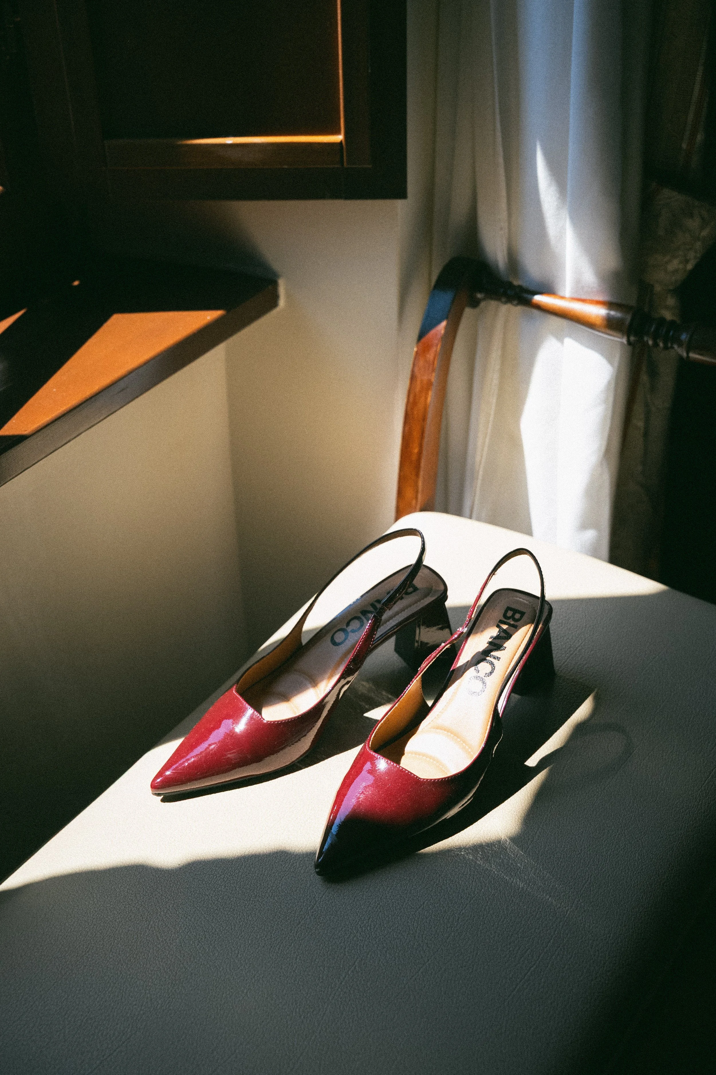 Paio di scarpe rosse con tacco alto su un tavolo bianco, con una luce che crea ombre sullo sfondo.