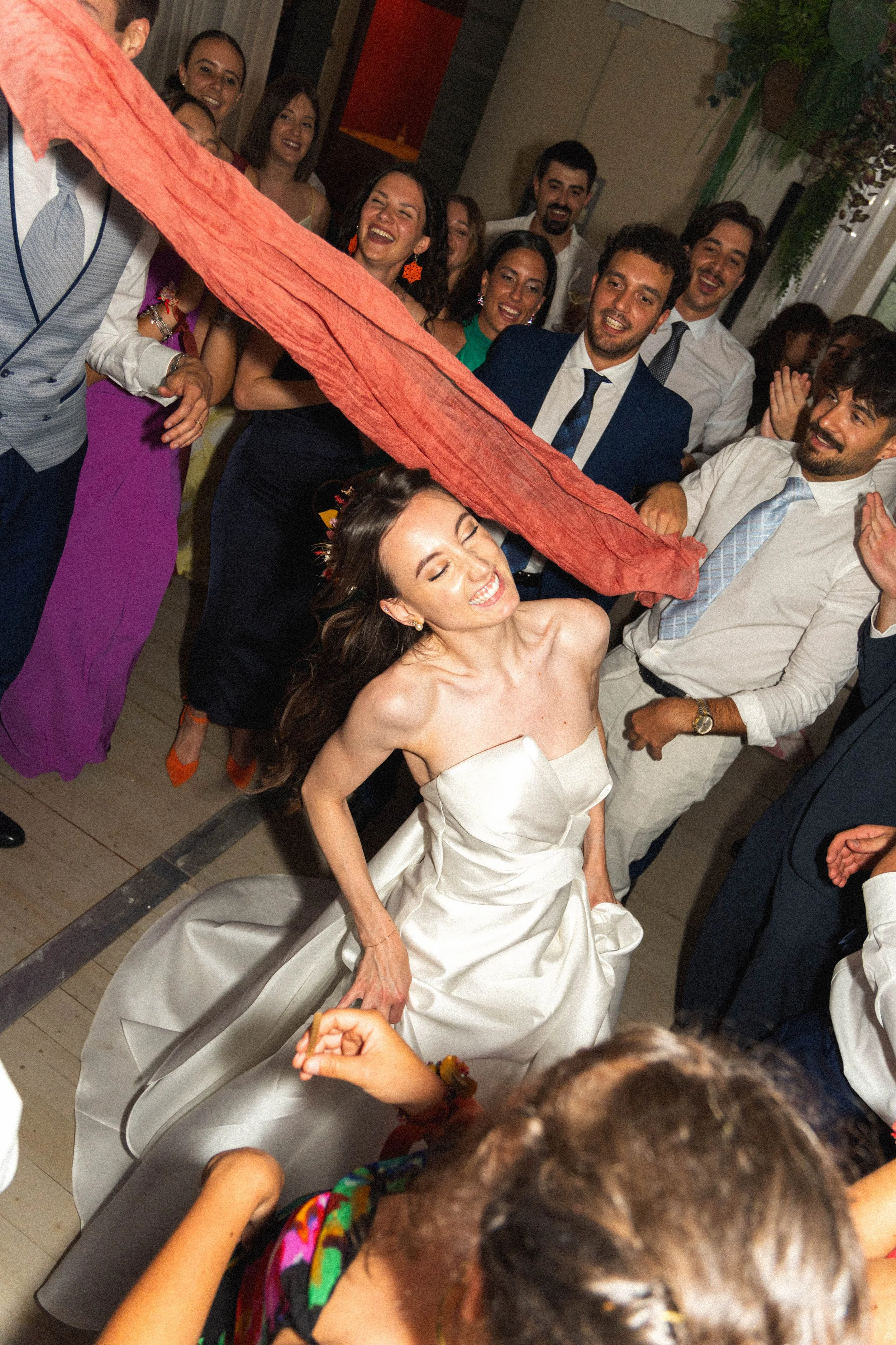 Una coppia di sposi, una donna in abito da matrimonio bianco e un uomo in abito scuro, ballano felici circondati da amici in un matrimonio festoso e allegro.