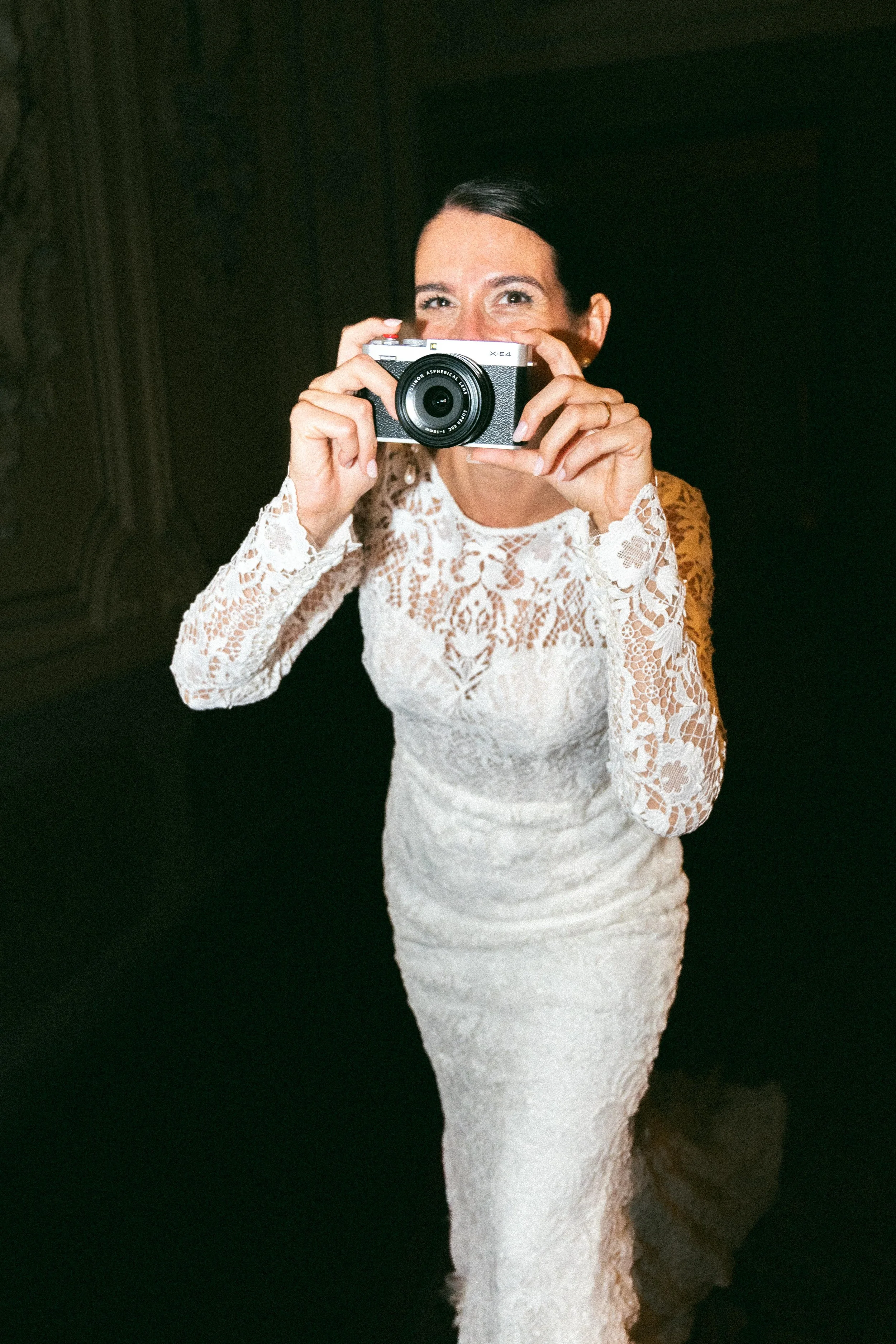 Una donna in abito lungo bianco in pizzo scatta una foto con una fotocamera