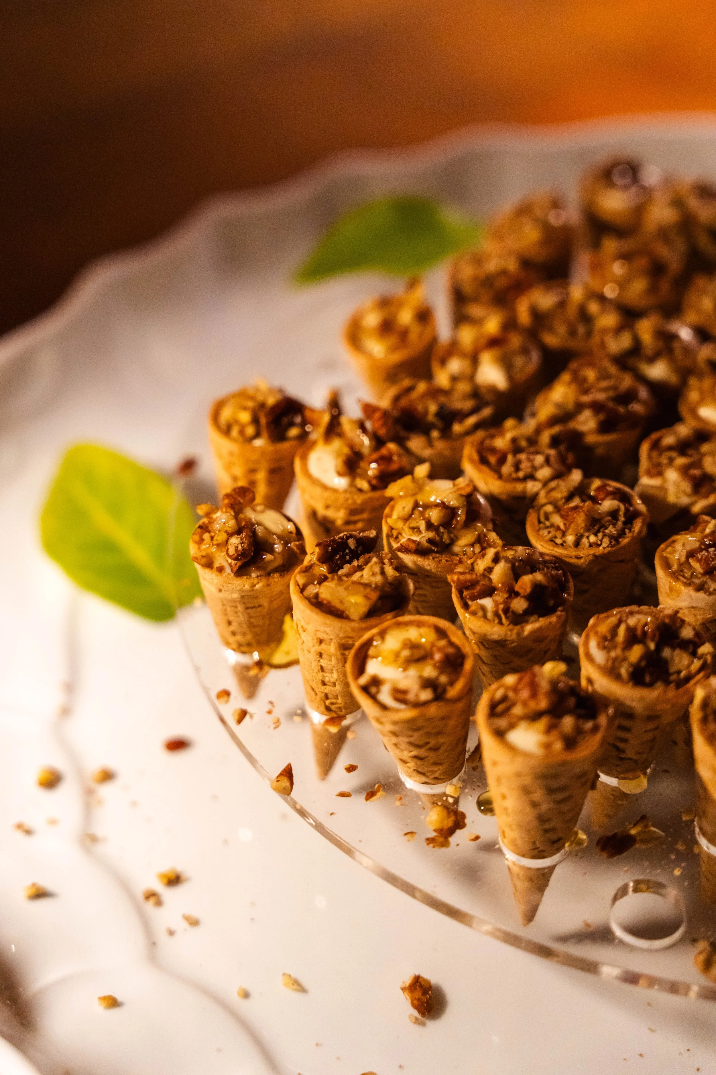 Cono di cialda riempito con crema e noci, decorato con foglie verdi, su un vassoio di vetro.