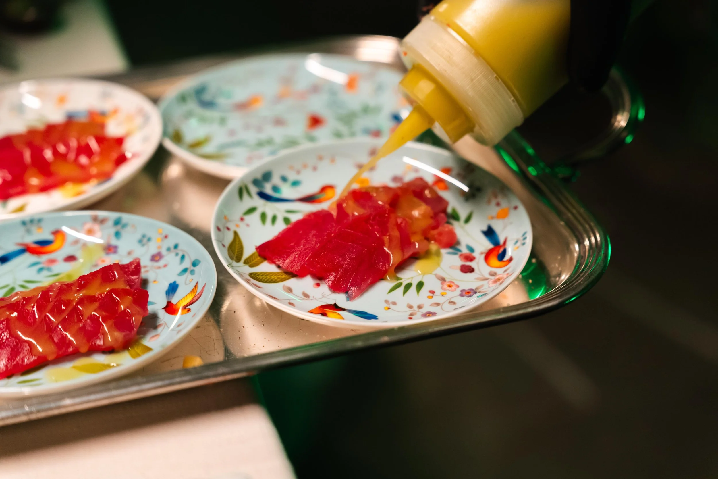 Tartare di pesce crudo servito in piatti decorativi con salsa gialla che viene versata sopra.