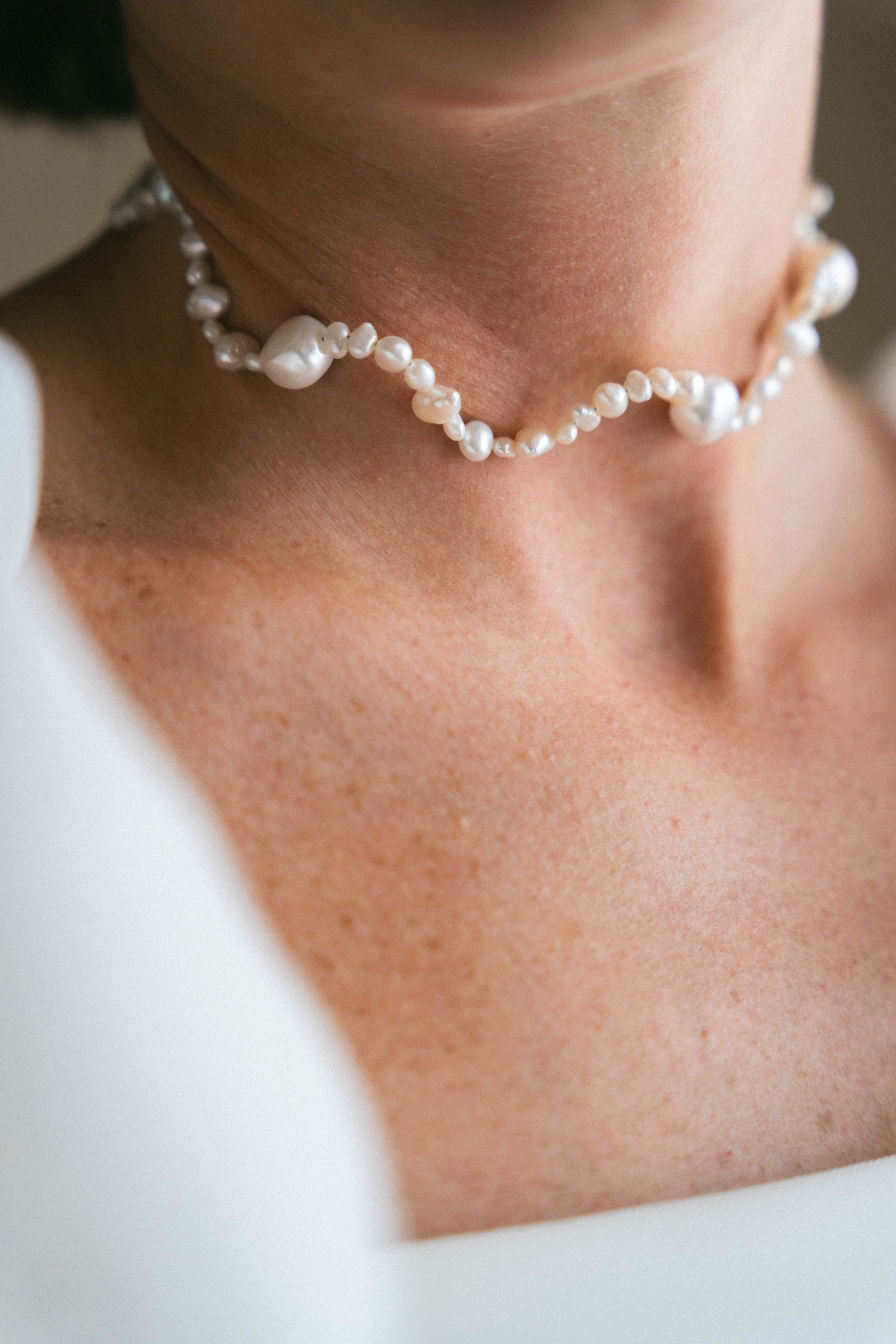 Gargantella di perle bianche intorno al collo di una persona, mostra solo il collo e parte del viso