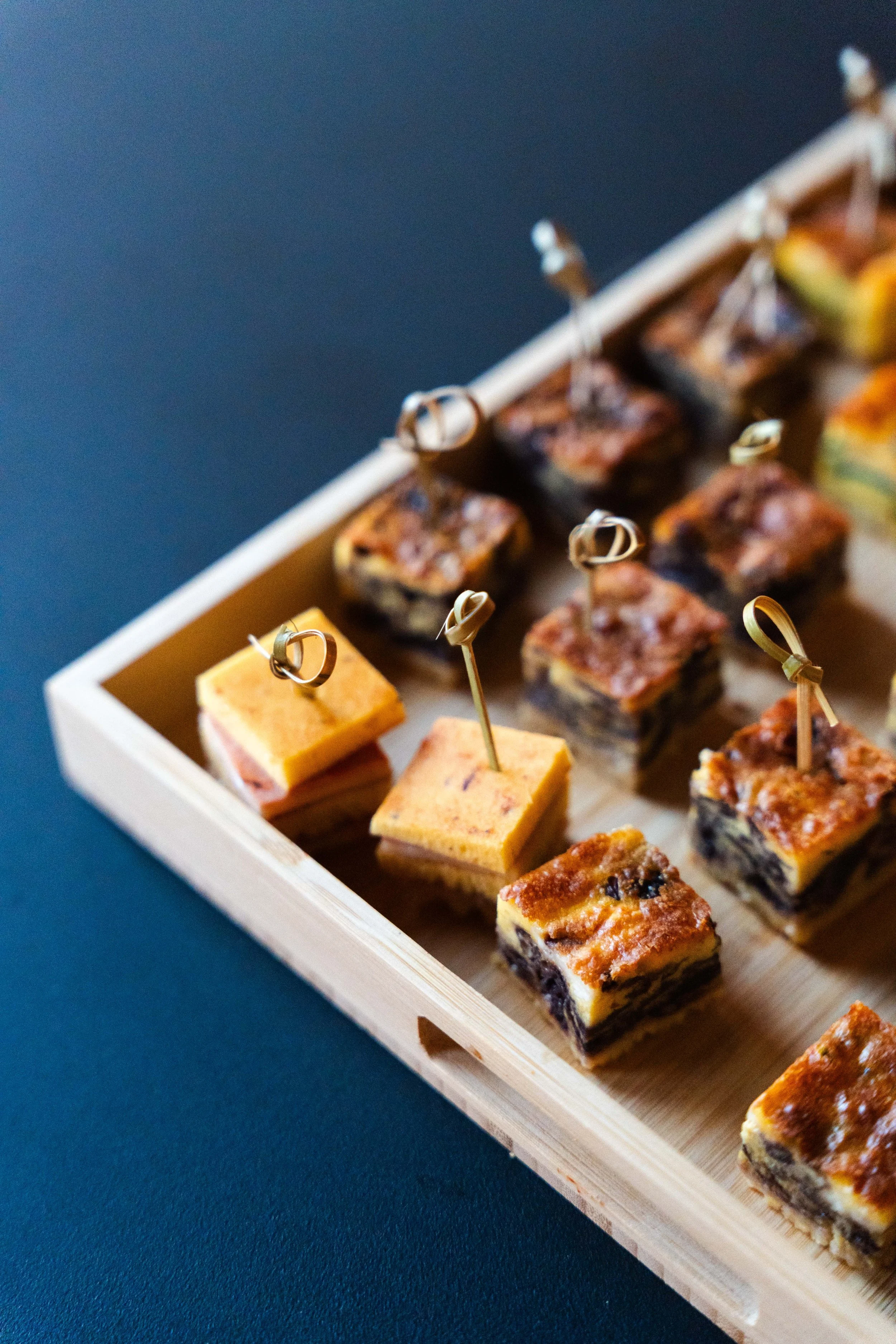 Assortimento di mini tartine salate servite in un piatto di legno.