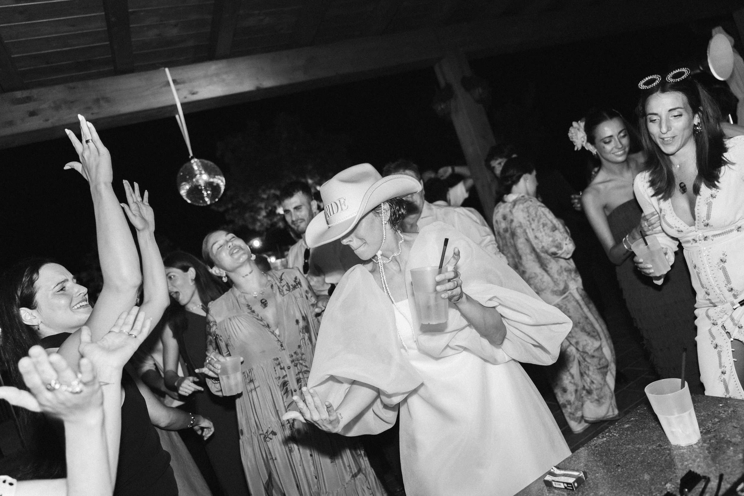 Un gruppo di persone che si divertono a una festa in un ambiente aperto, alcune di loro stanno ballando e altre stanno sorseggiando bevande.
