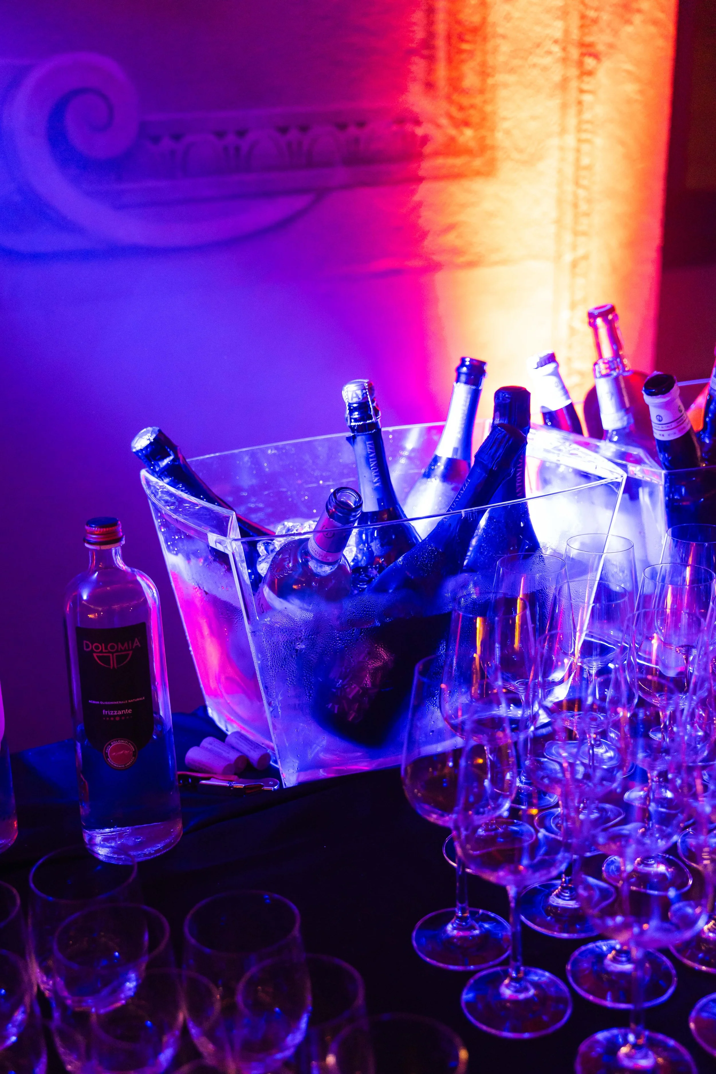 Bottiglie di alcolici e bicchieri di vino in un ambiente festivo con luci colorate NEON