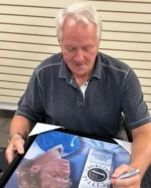 Darryl Sittler signing a photograph of himself at a table.