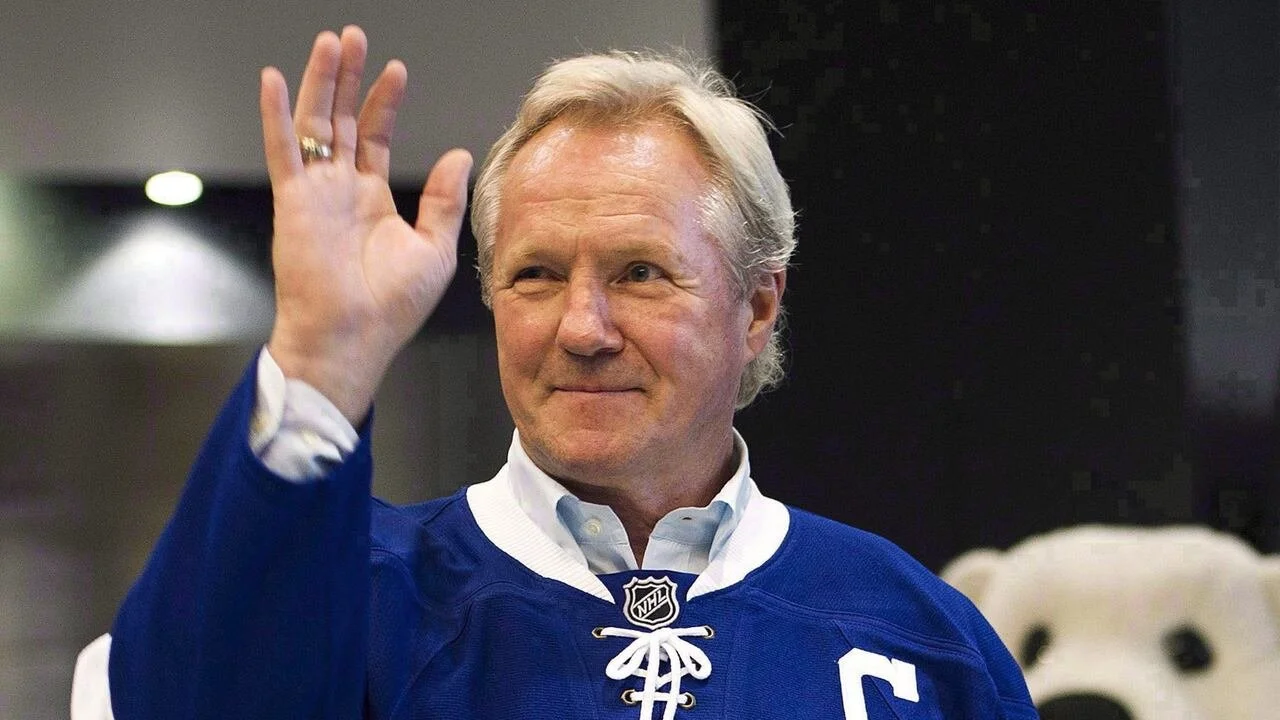 Darryl Sittler with white hair waving, wearing a blue hockey jersey with a white shirt underneath