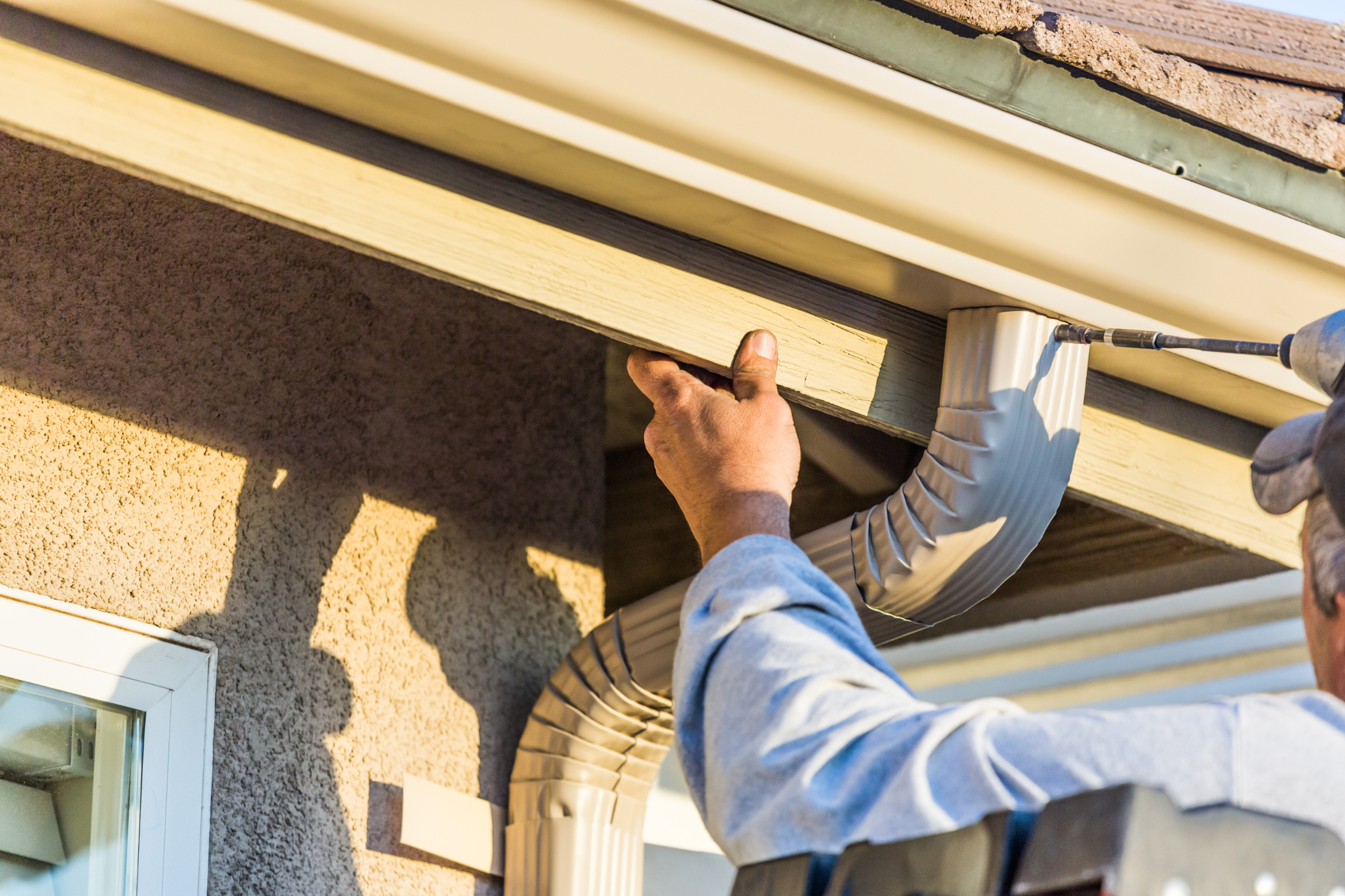 Worker installing or inspecting a vent pipe under the roof eaves of a house.