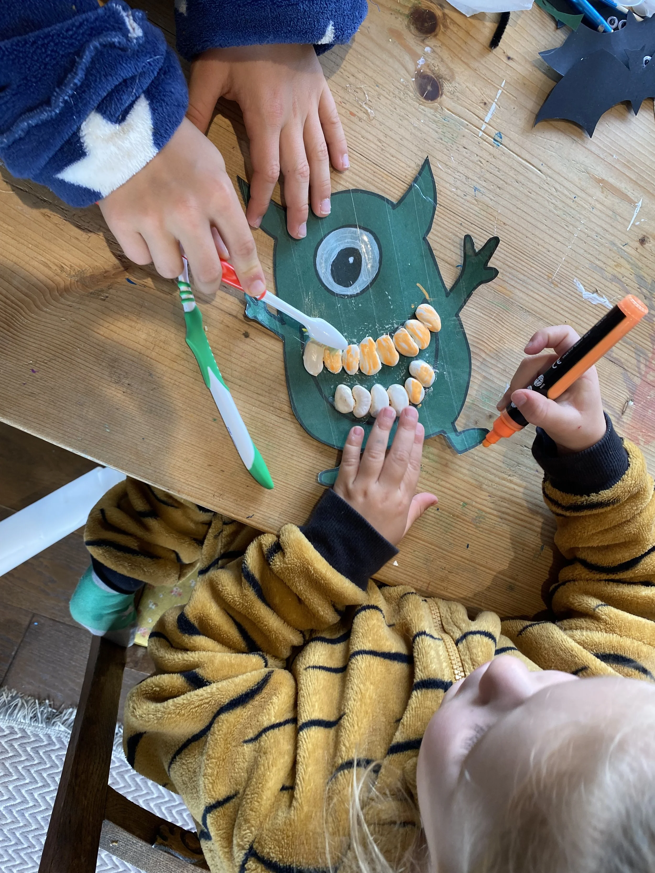 Children decorating a Halloween monster craft with frosting and candies on a wooden table.
