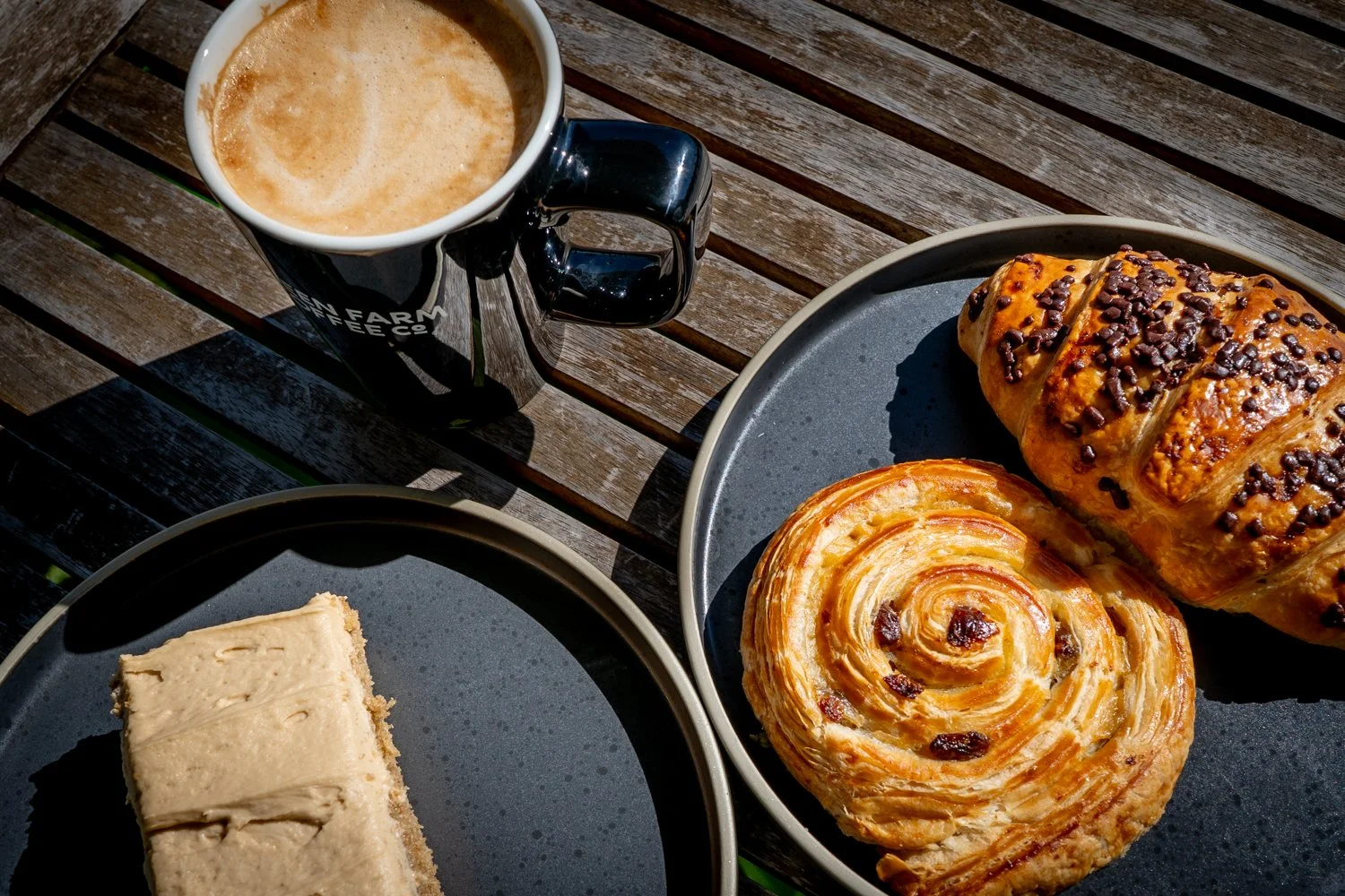 Selection of pastries and cake on black plates sat on a wooden table outside