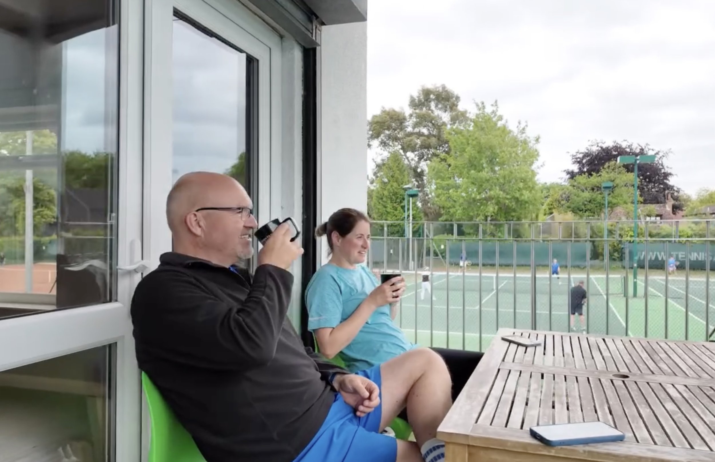 A male and a female enjoying a drink, watching tennis from the balcony