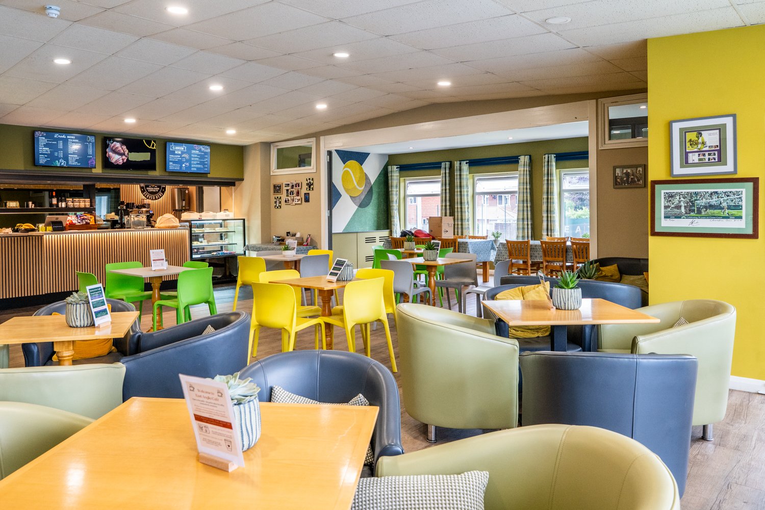 Club bar and cafe.  Lots of tables and chairs, with a mix of soft grey chairs and then harder green and yellow chairs.  The room is brightly lid and welcoming.