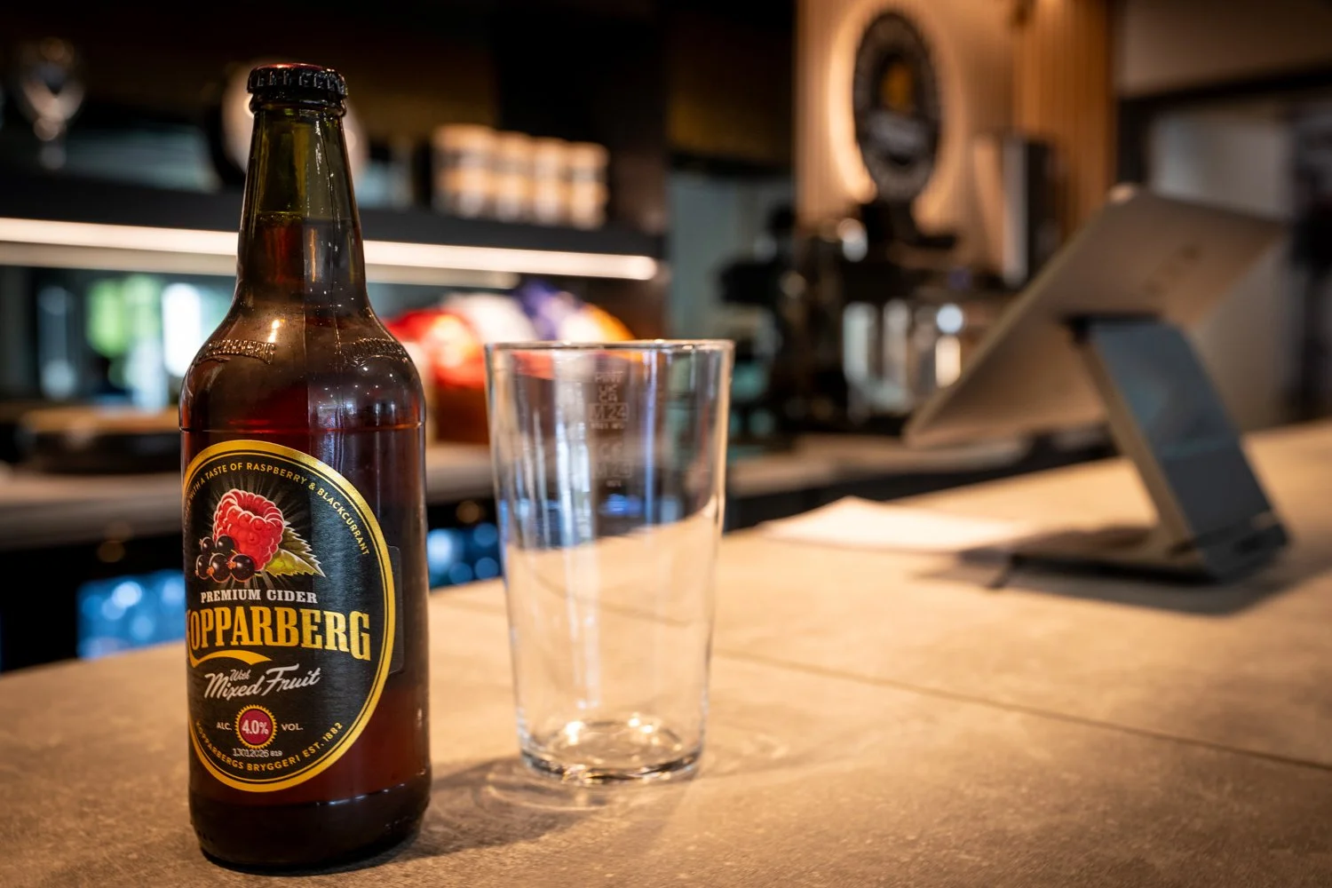 Bottle of cider with a glass, resting on a the bar counter