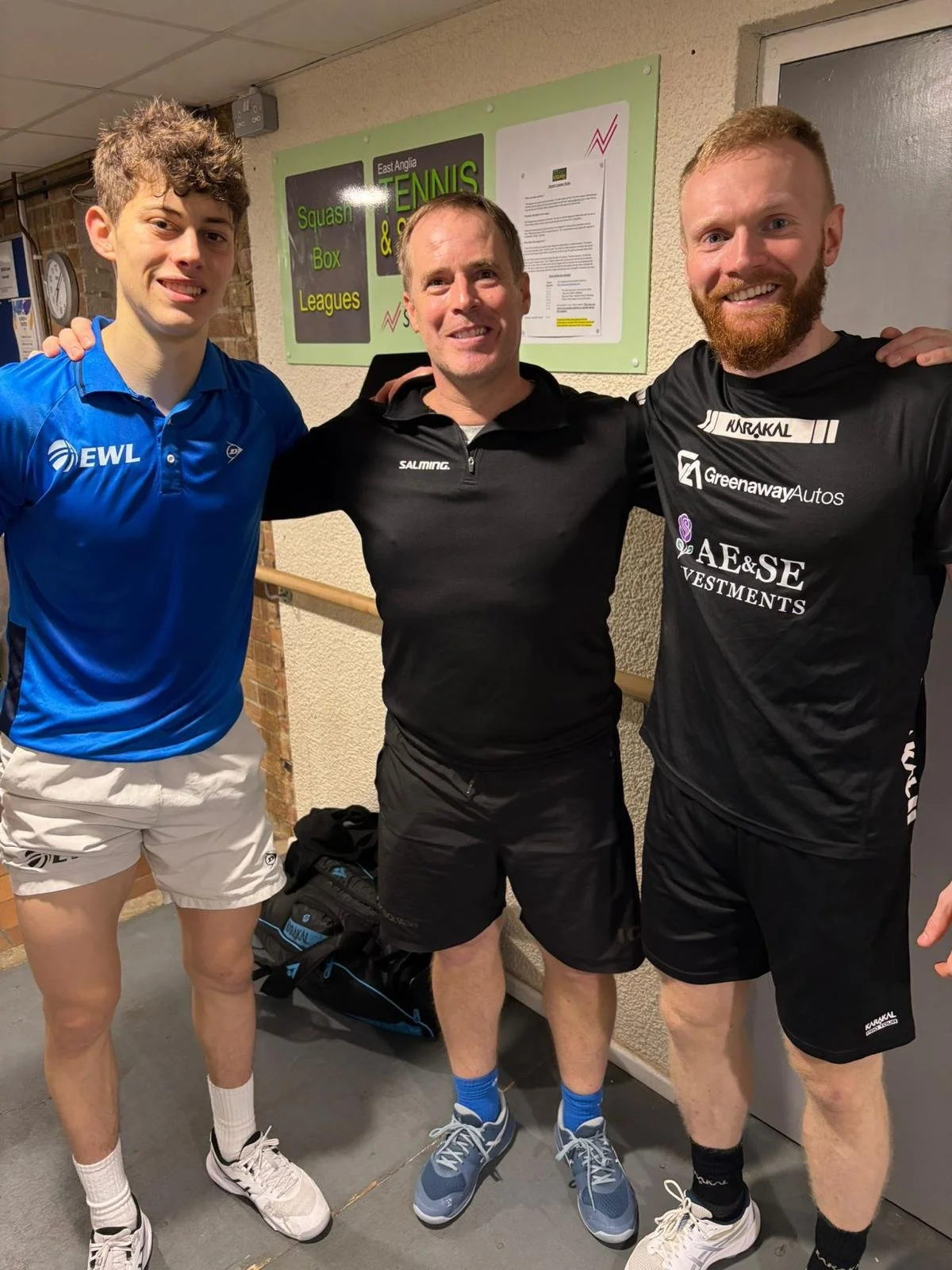 3 male squash players arms around shoulders smiling at the camera