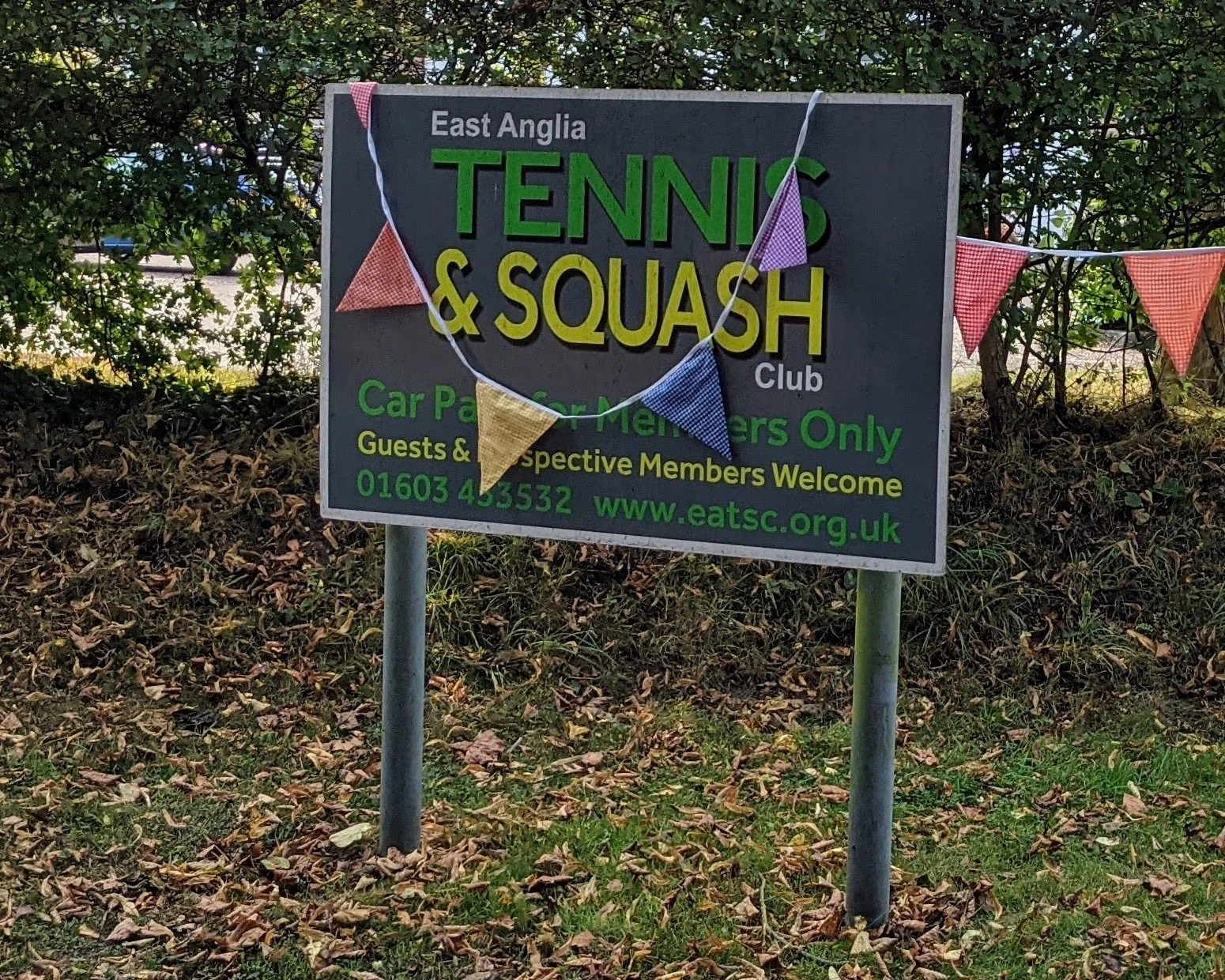 Sign welcoming people to the club, set in the grass with a hedge behind