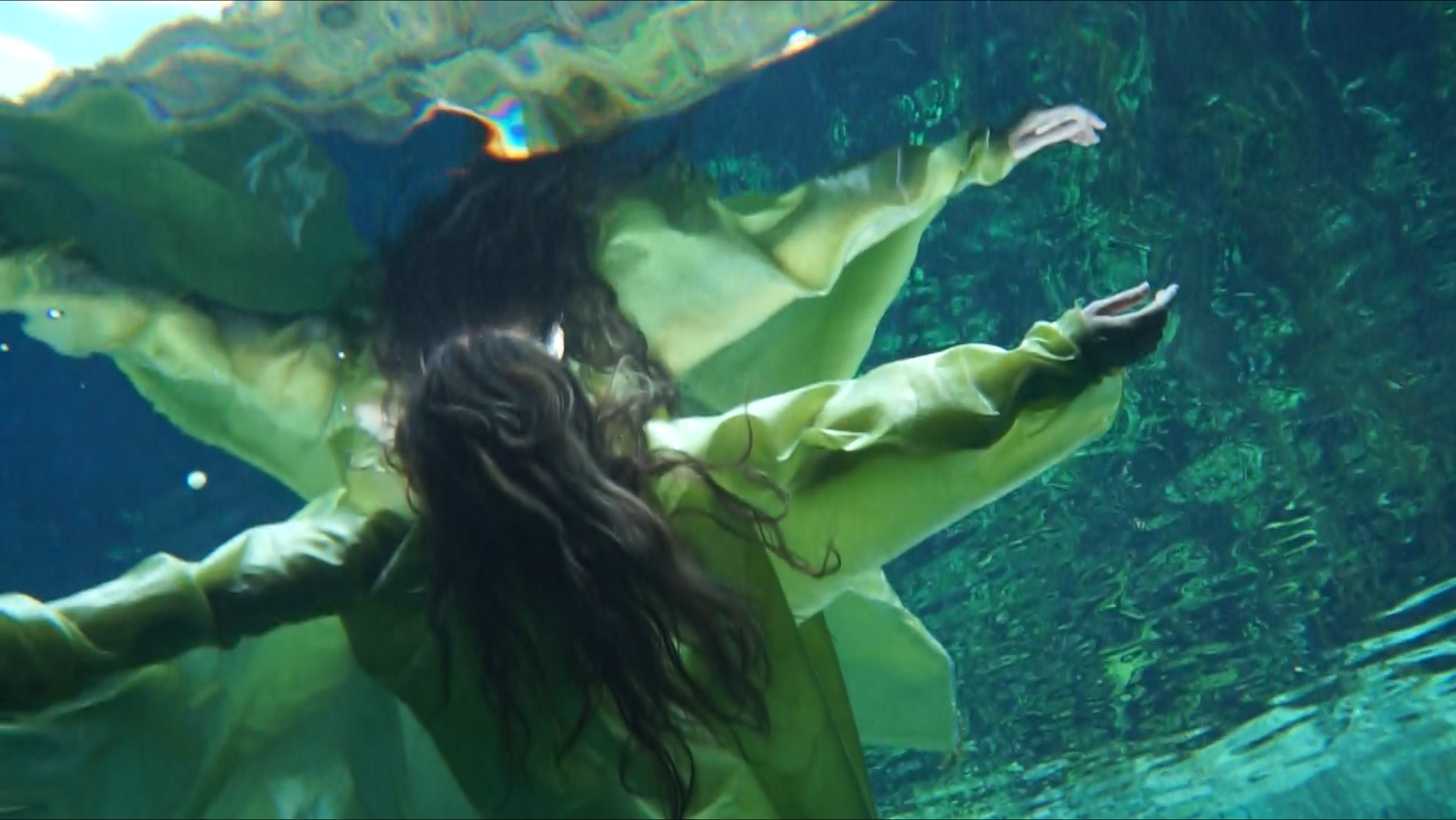 figure in light green floating in water seen from below