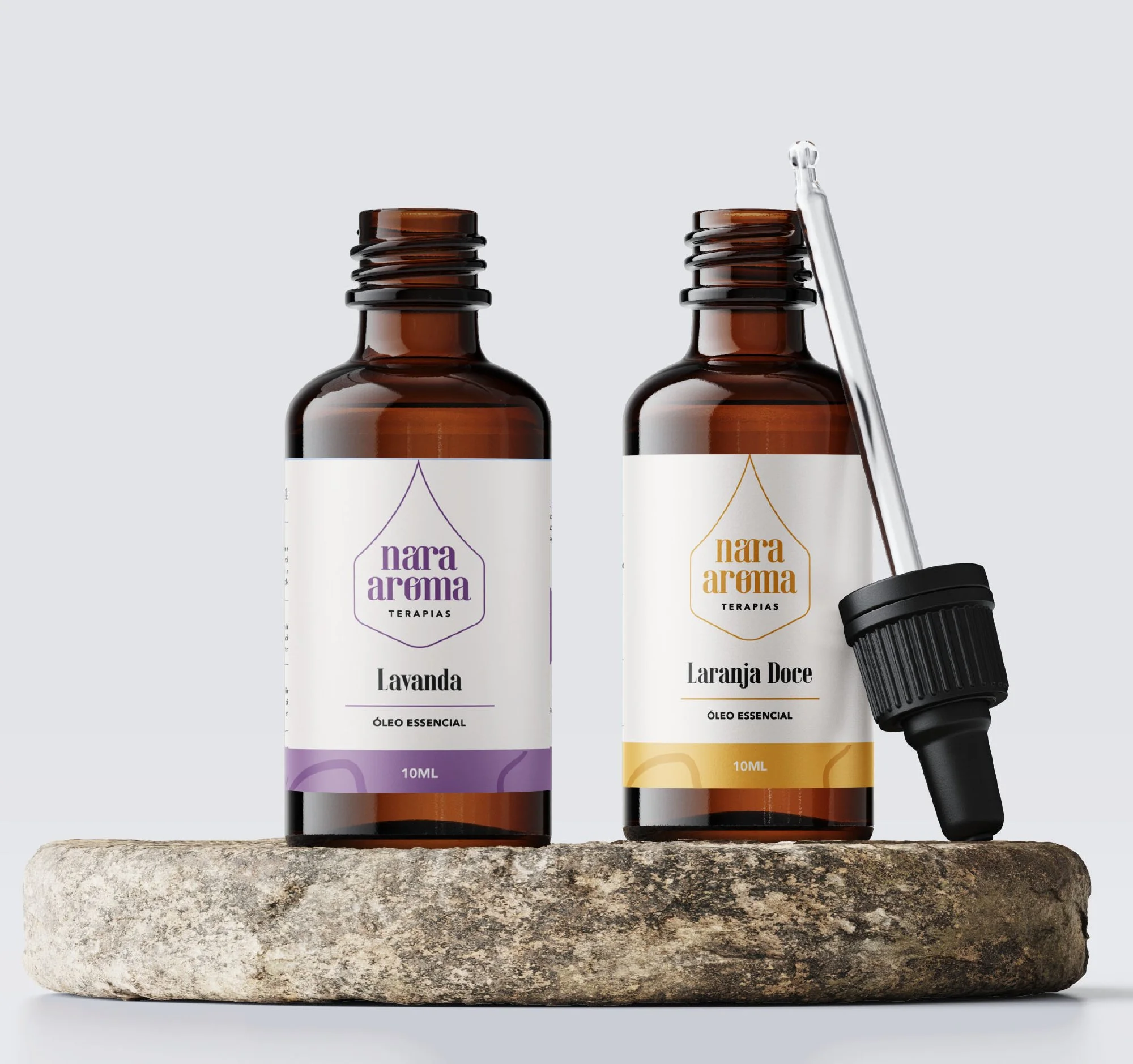 Duas garrafas de óleos essenciais com rótulos de Lavanda e Laranja Doce, uma com conta-gotas ao lado, sobre uma pedra cinza.