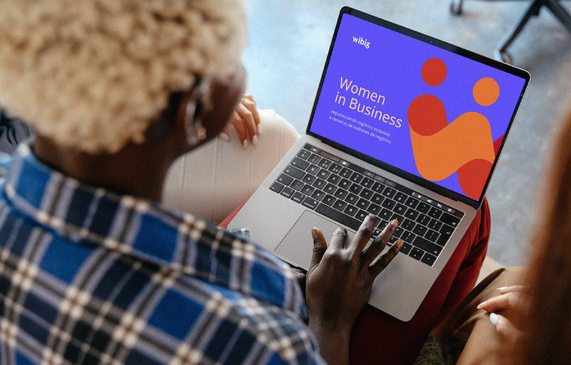 Pessoa com cabelo dourado usando uma blusa de camadas azuis, sentado segurando um laptop com tela que mostra o título 'Women in Business' e cores vibrantes.