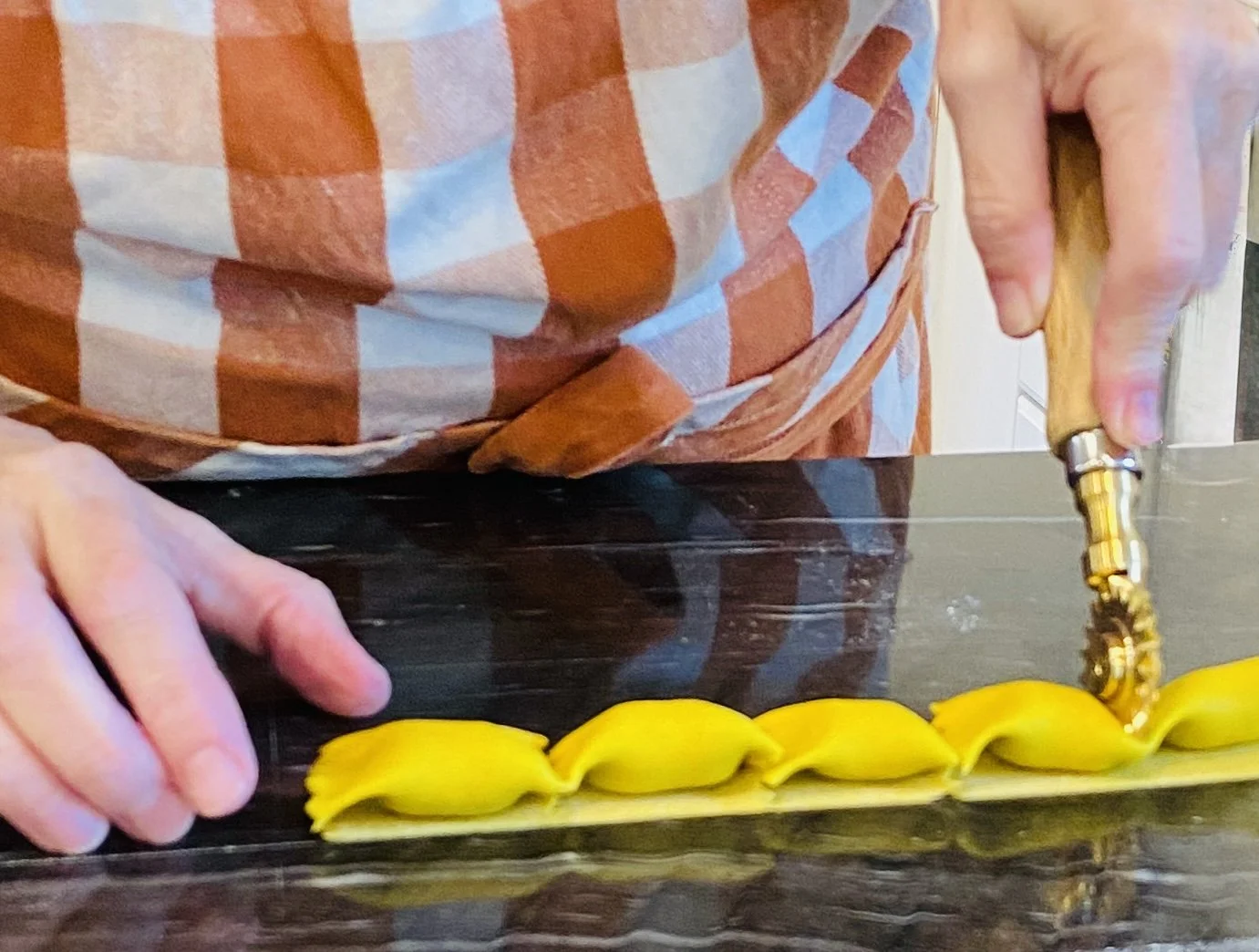 Person slicing pasta dough on a dark kitchen countertop with a knife.