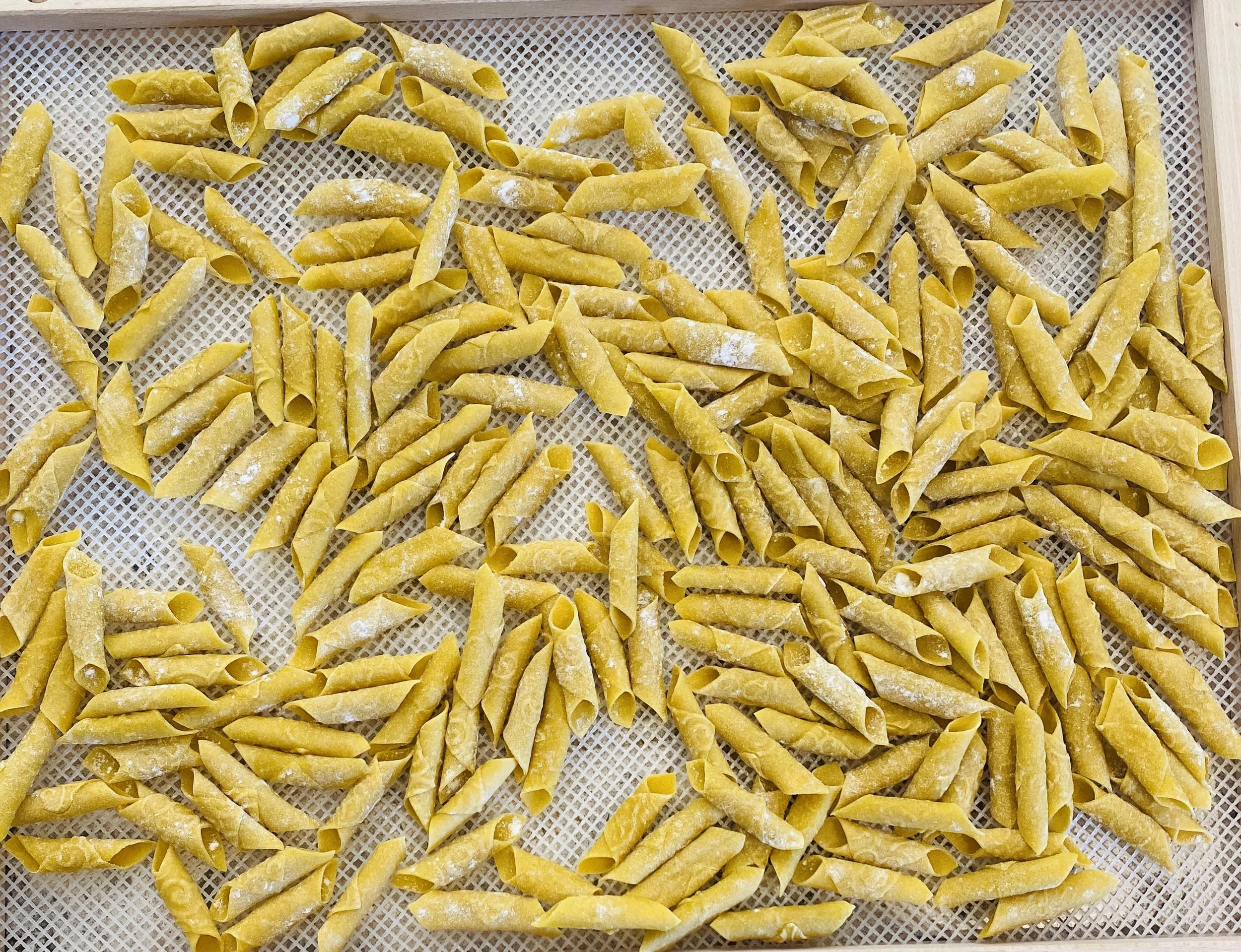 Uncooked yellow pasta tricolor fusilli with folded and twisted shapes on a mesh tray.