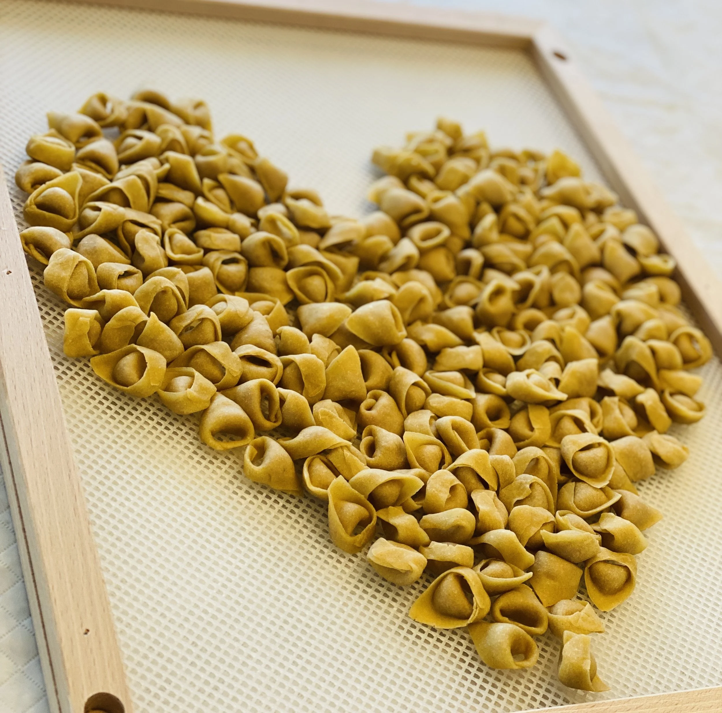 Trailing bunches of dried tortellini pasta on a white mesh tray.