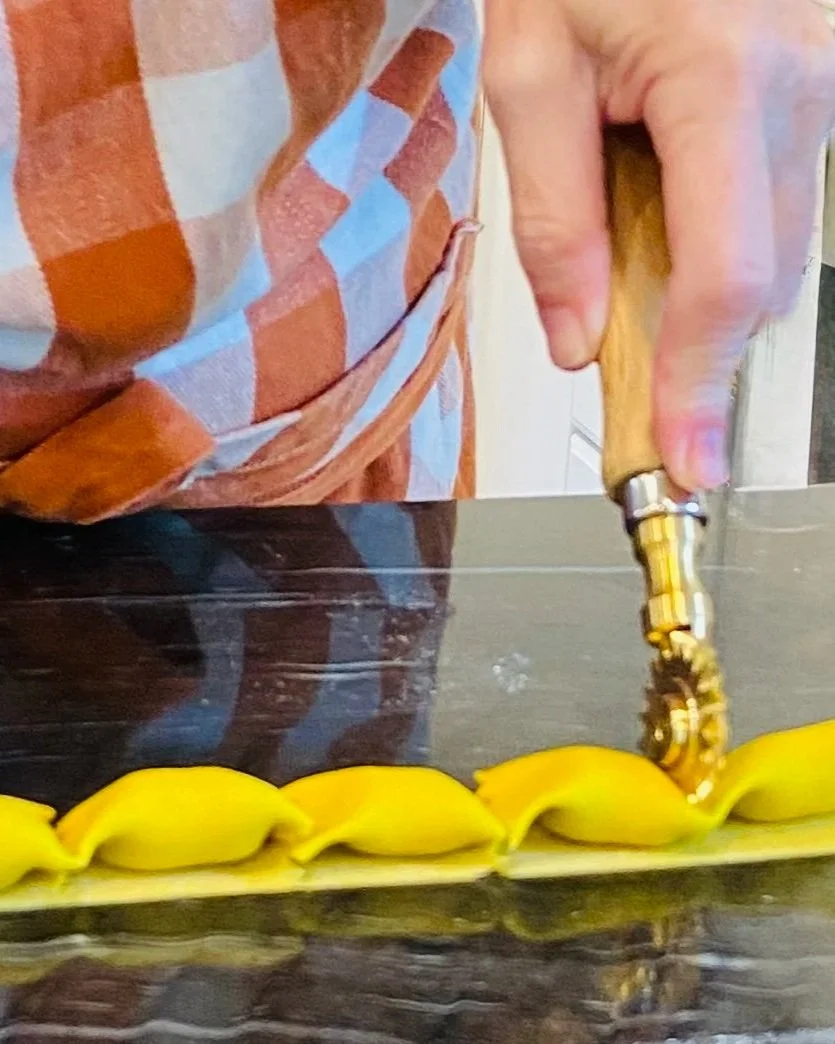 Person slicing pasta dough on a dark kitchen countertop with a knife.