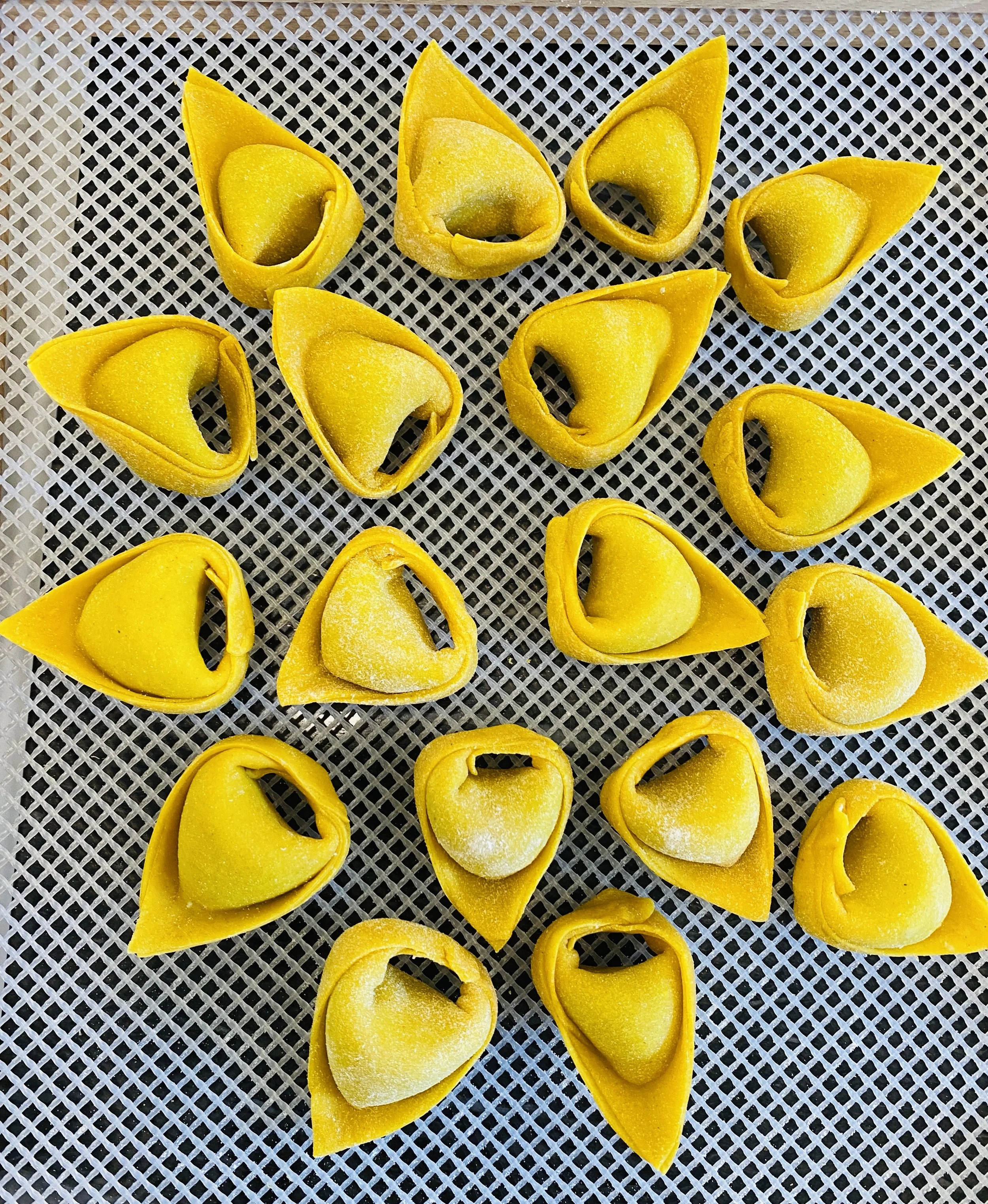 Several yellow tortellini pasta pieces on a gray textured surface, some with a light dusting of flour.