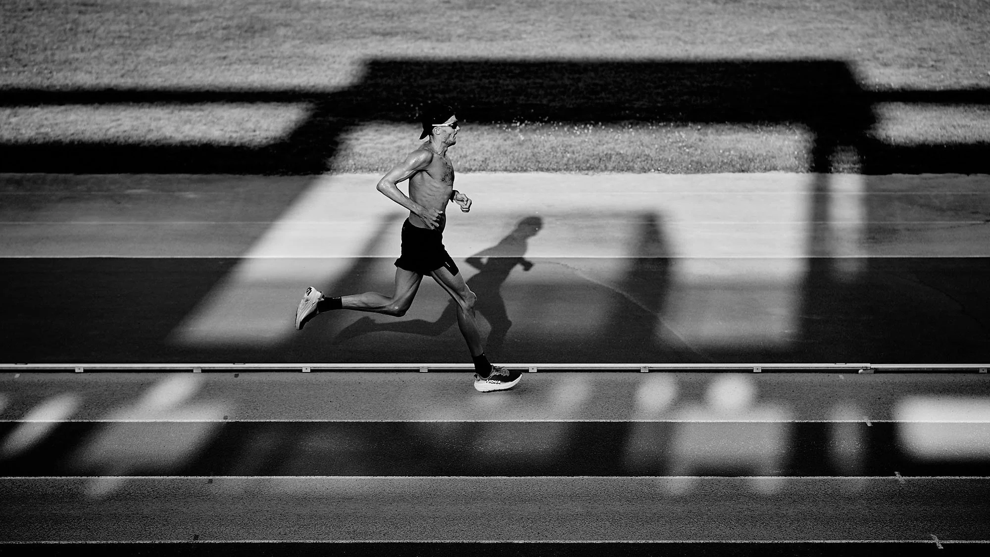 Jan Frodeno running on a track, with his shadow cast on the ground. The photo is taken from an overhead perspective and is in black and white.