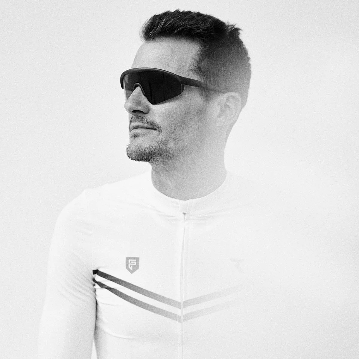 Man wearing reflective sports sunglasses and a white athletic jersey with black and gray stripes, looking to the side, against a plain white background.