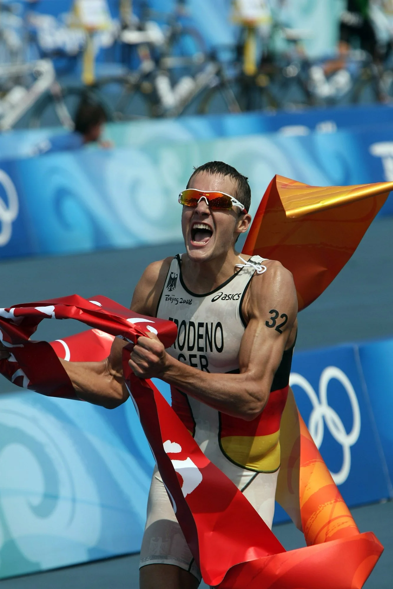 Jan Frodeno celebrates crossing the finish line at the 2008 Olympics in Peking, holding the German flag aloft with joy.
