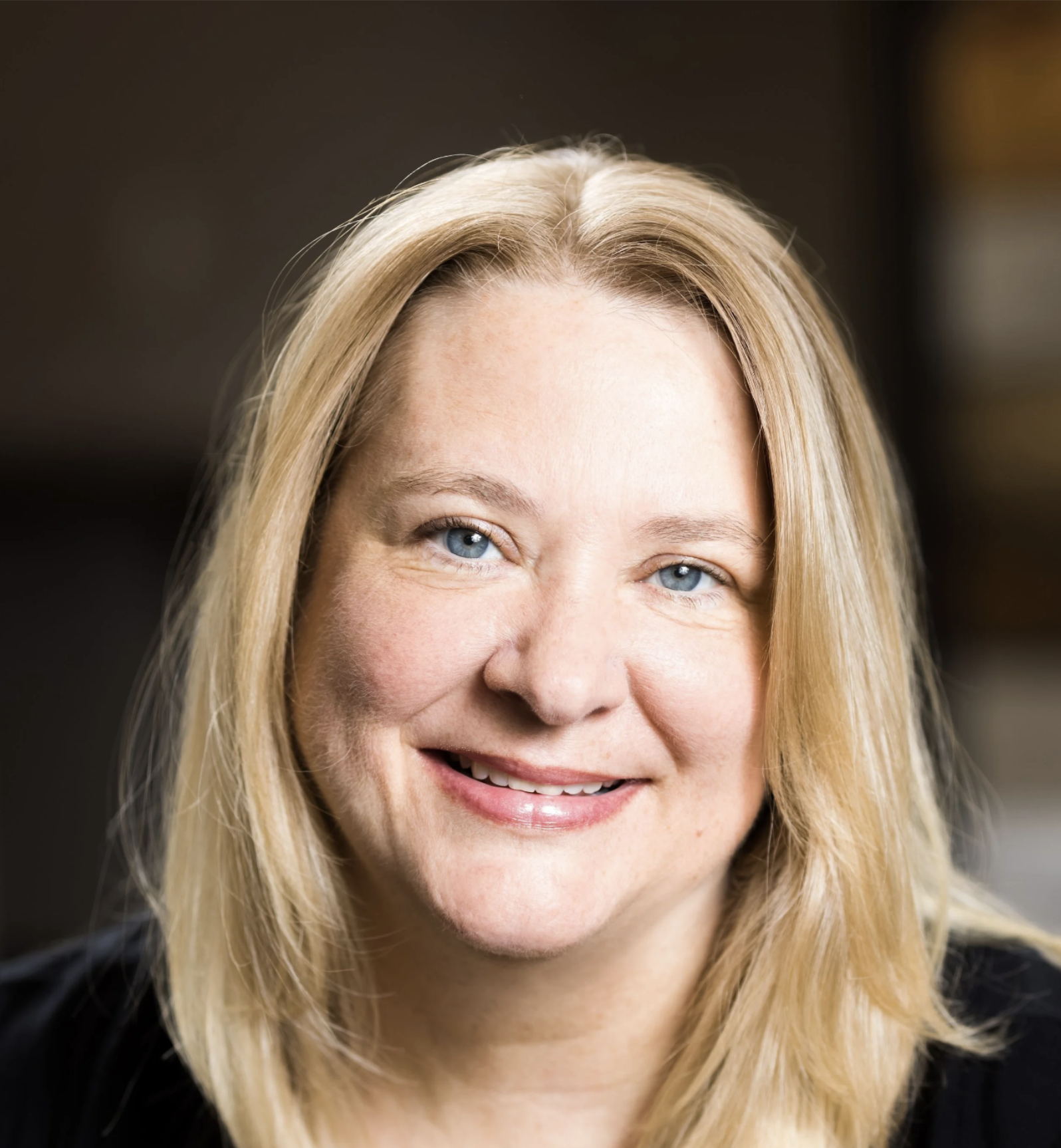 Close-up portrait of a smiling woman with blonde hair and blue eyes.