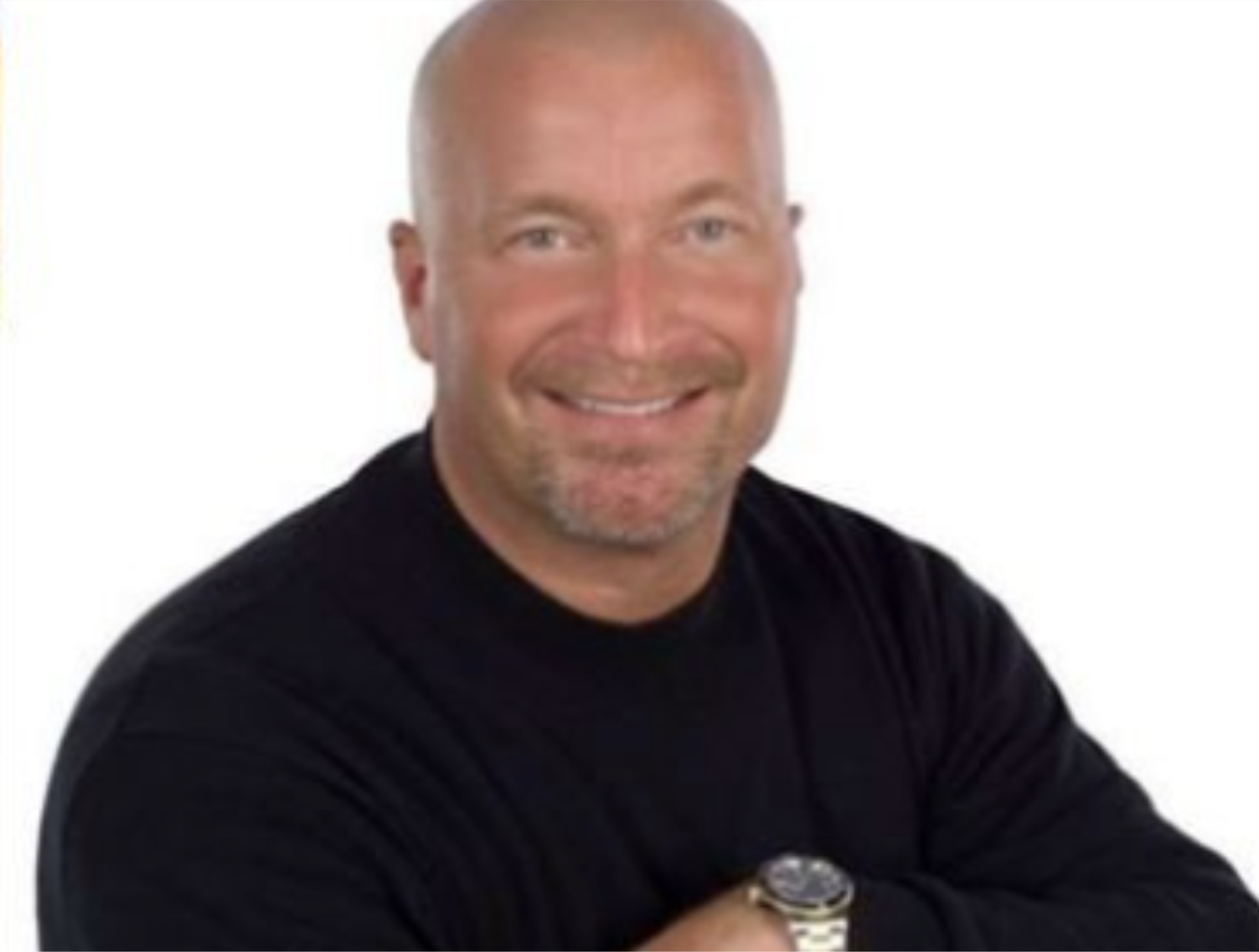 A smiling man with a bald head, light beard, wearing a black shirt and watch, against a white background.