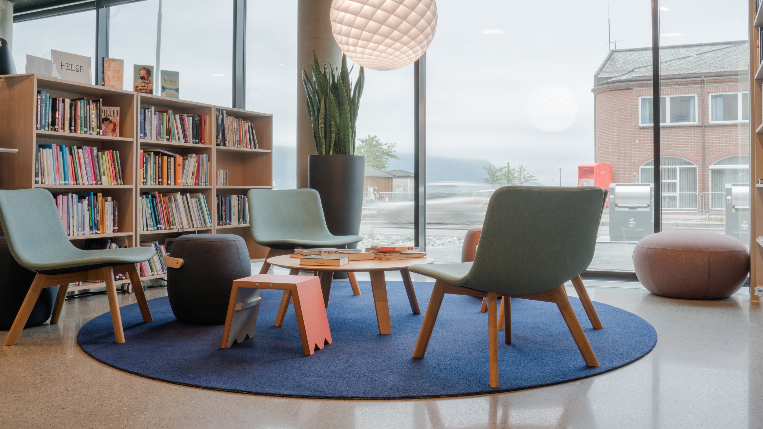 Foto: Cecilie Hatløy, Møre Media AS. Moderne sittegruppe. Bibliotek, helse. Innendørs leserom med bokhyller, lenestoler, et lite bord med bøker, og store vinduer og et utendørsområde.