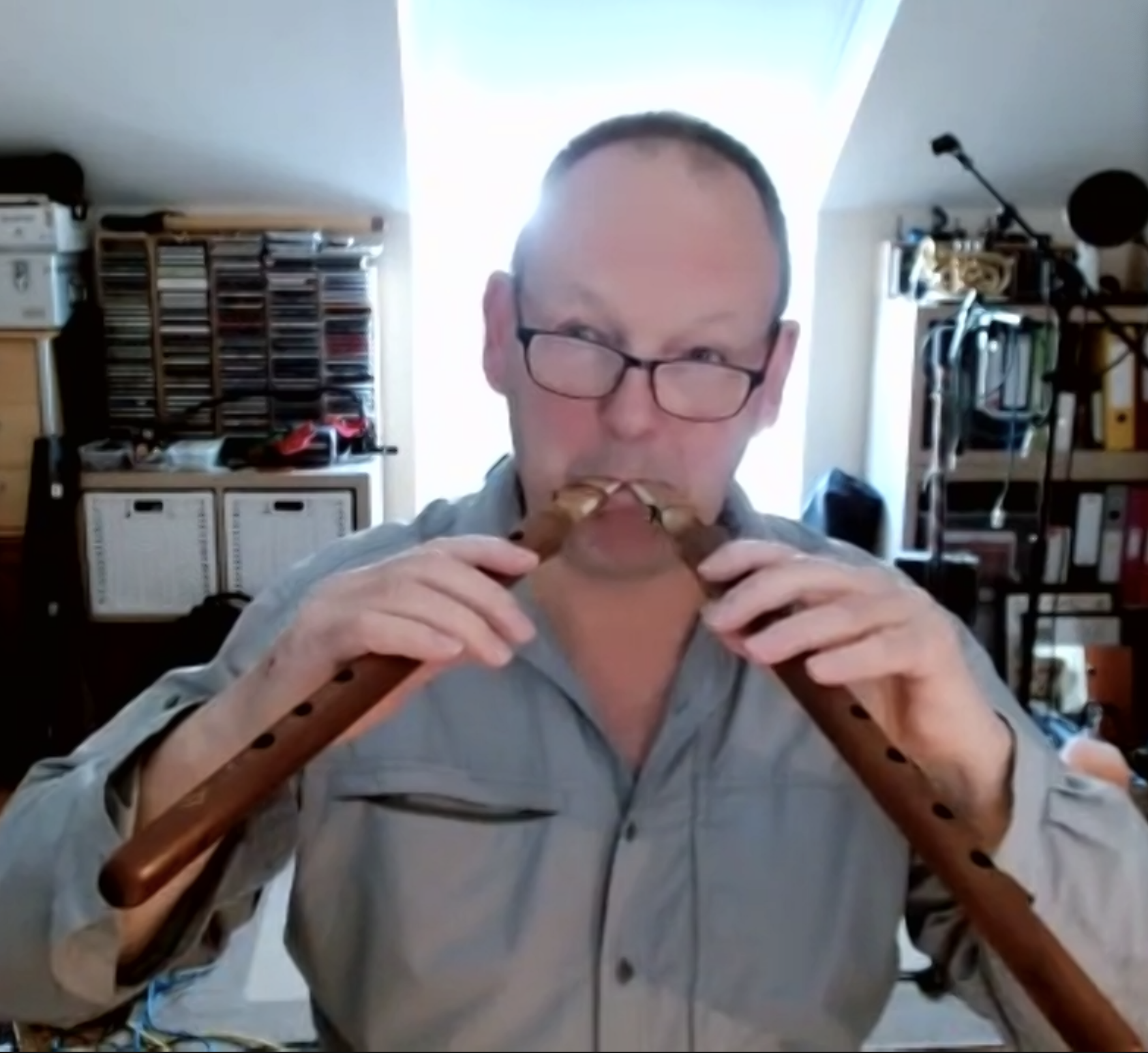 A man wearing glasses playing a wooden flute.