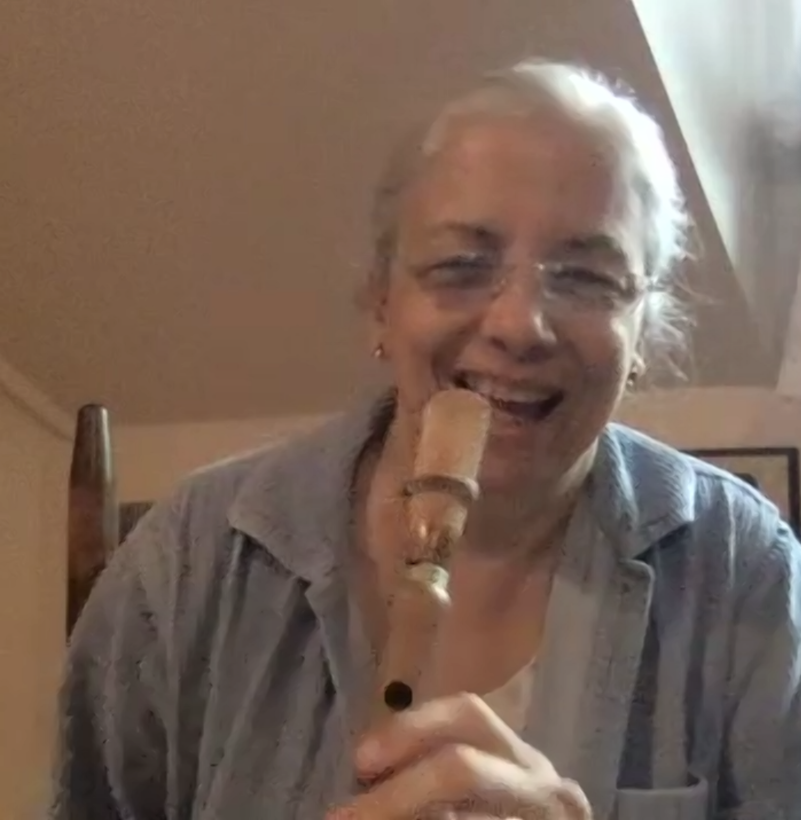 An elderly woman smiling and holding a wooden stick with a small ceramic figure on top.