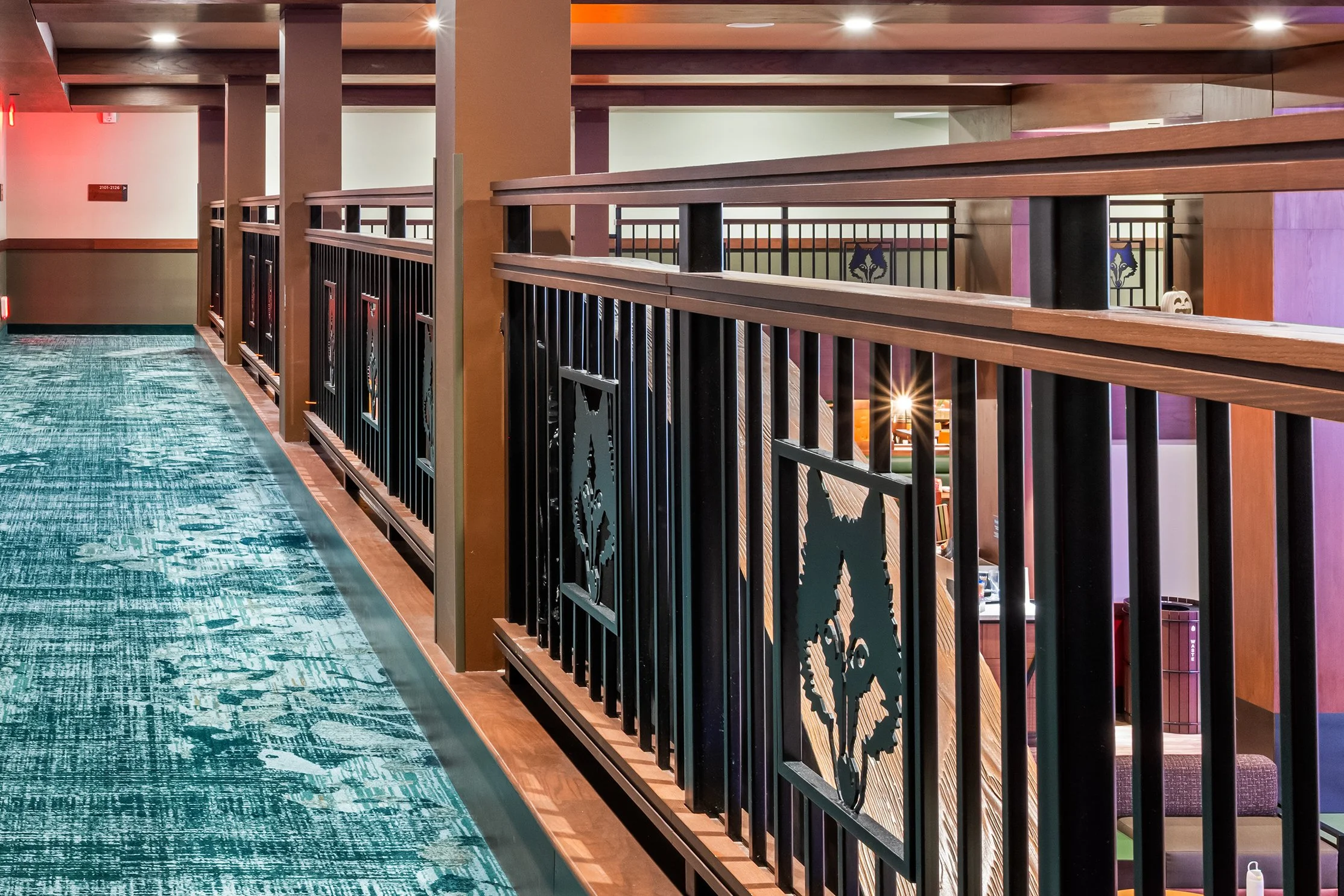 Indoor view of a hotel or casino upper level balcony with black and wood railings featuring horse or unicorn motifs, a teal patterned carpet, and colorful walls.