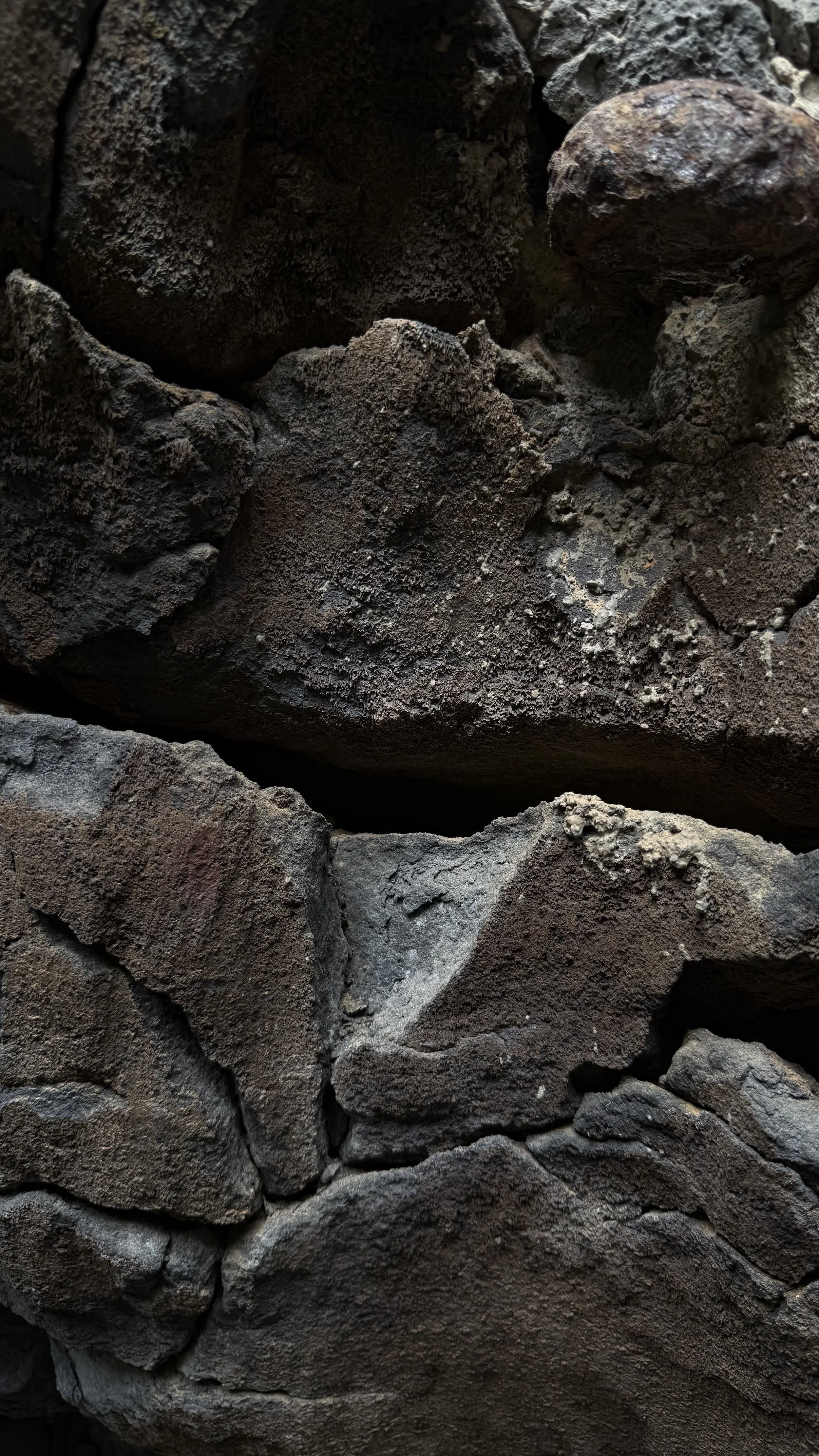 Close-up view of rough, dark gray and brown rocks embedded in concrete or stone wall.