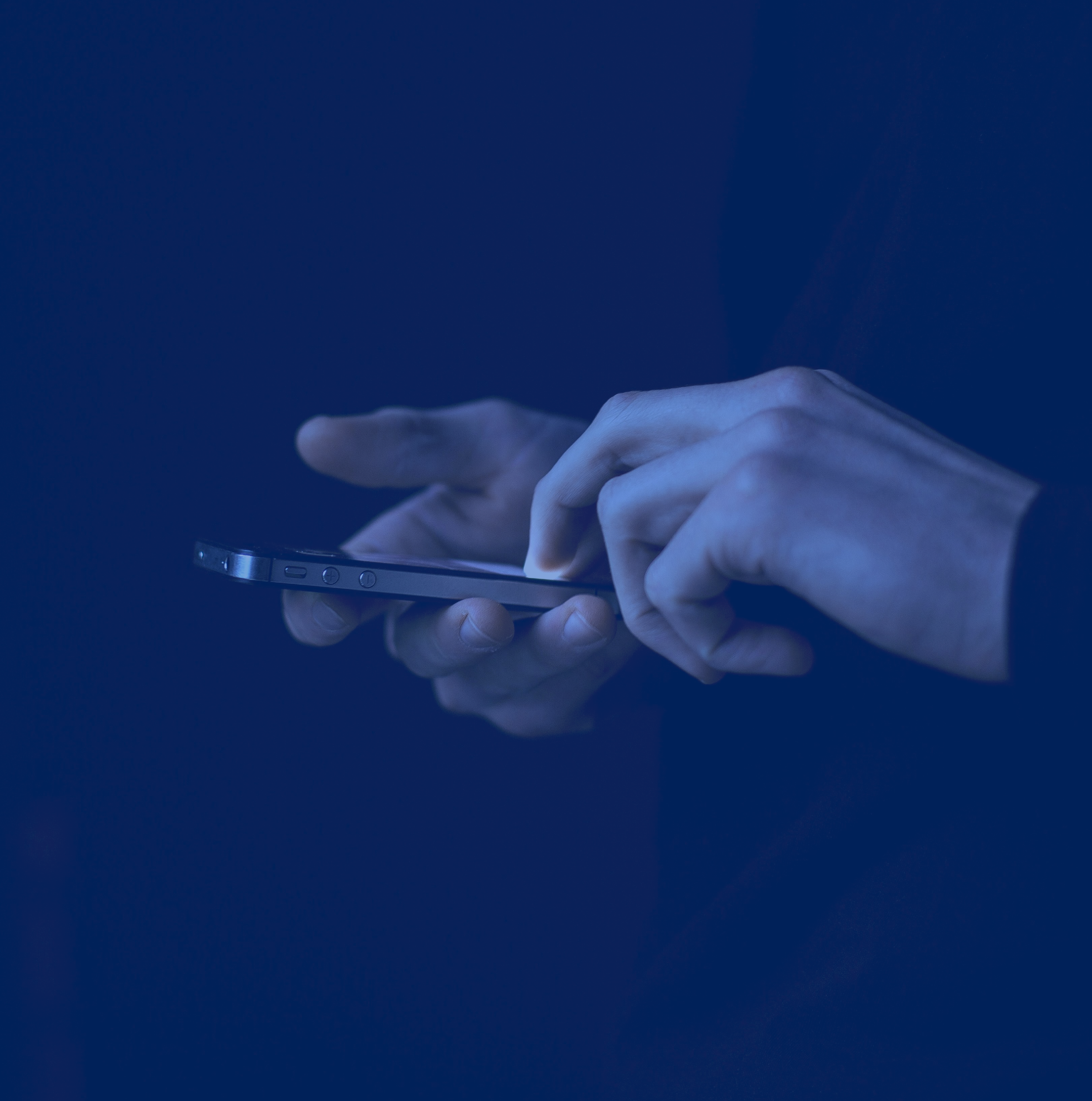 Close-up of a person's hands using a smartphone in a dark setting.
