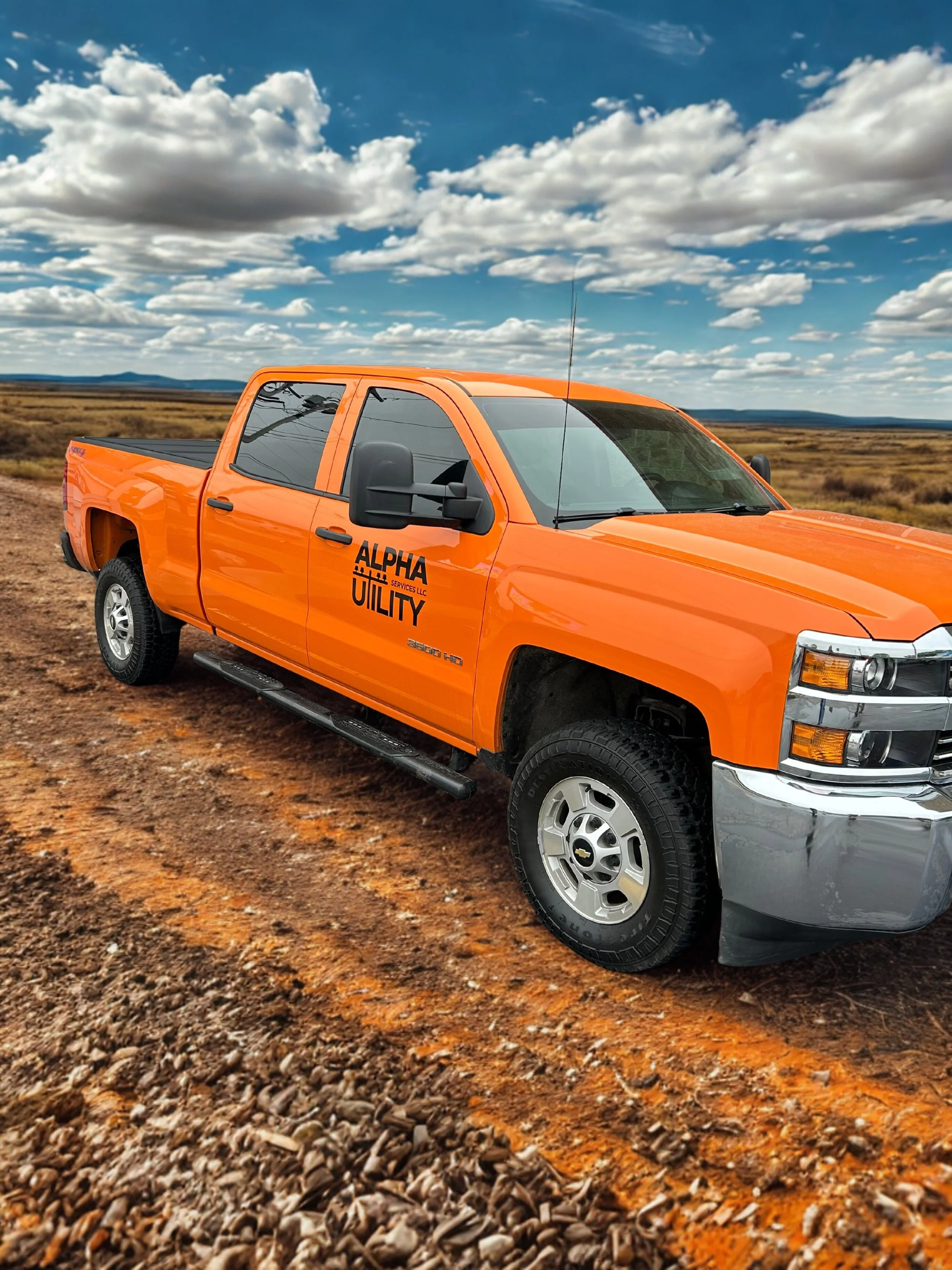 Orange pickup truck parked on dirt road in open landscape under cloudy sky