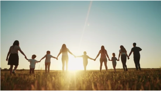 Group of people holding hands and standing in a field during sunset.
