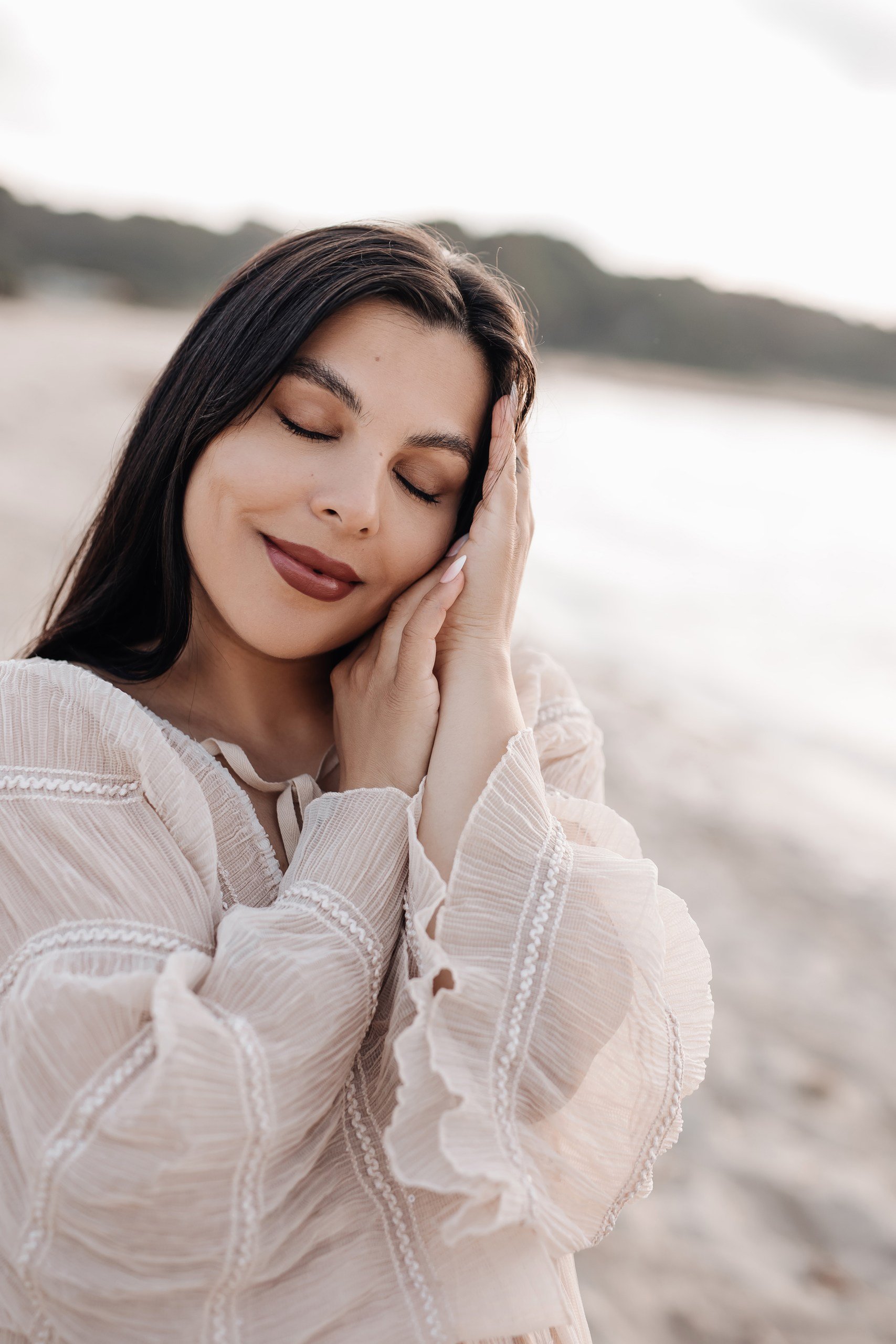 Eine glückliche Frau mit geschlossenen Augen und einem Lächeln am Strand bei Sonnenuntergang