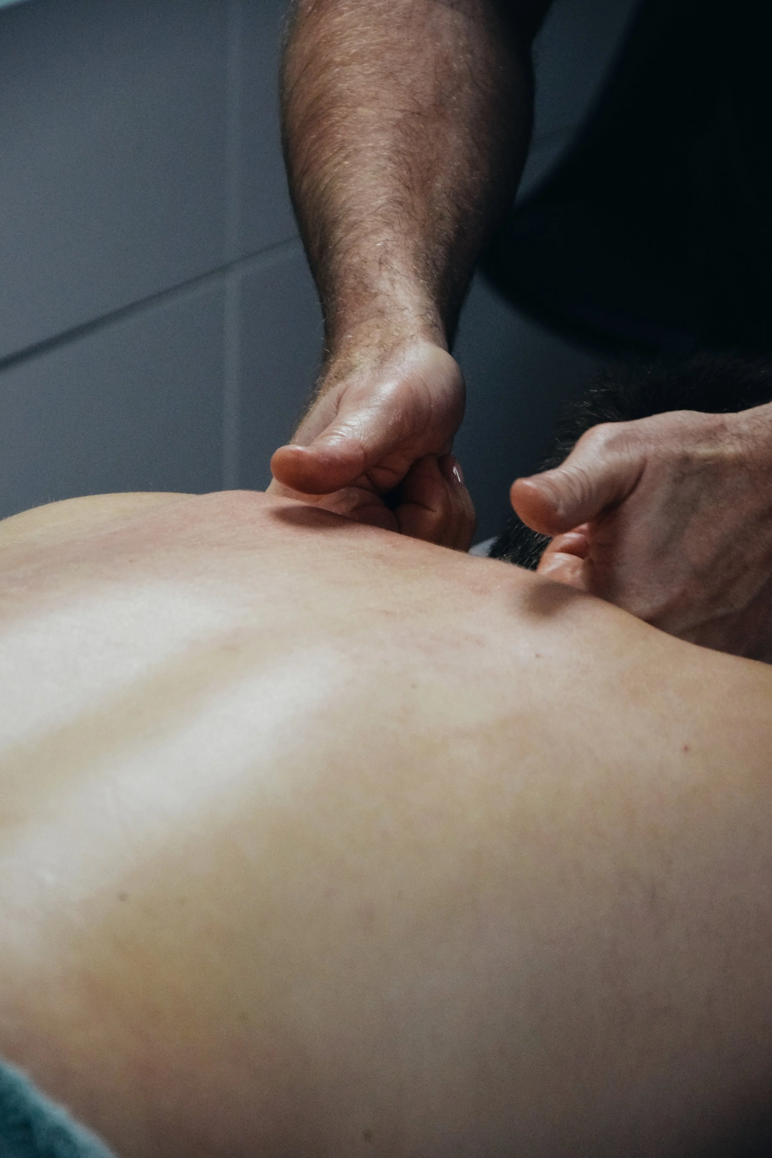 A massage therapist performing a massage on a person's back with the therapist's hands and forearms visible.