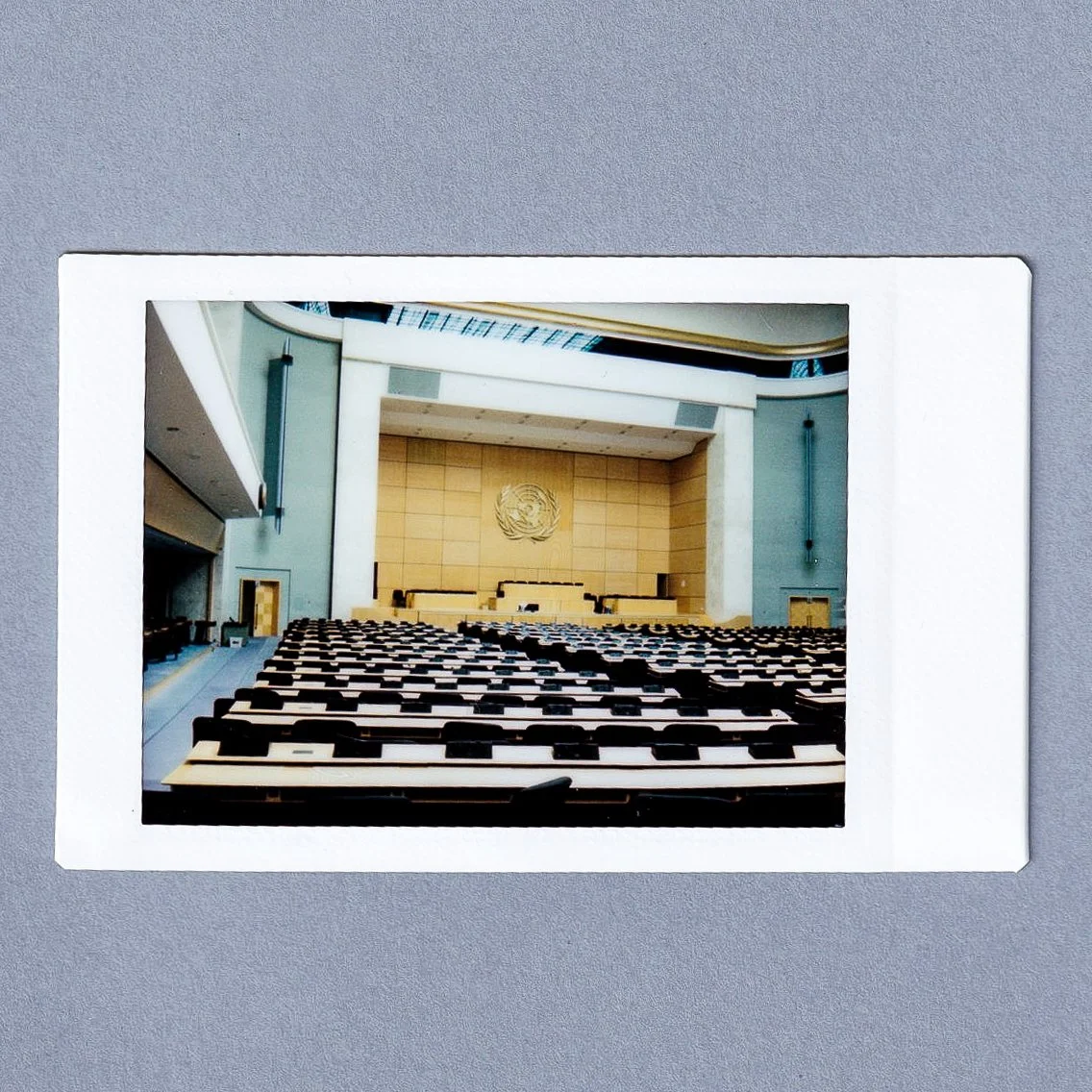 The interior of a United Nations conference room with rows of seats facing a stage with the UN emblem.